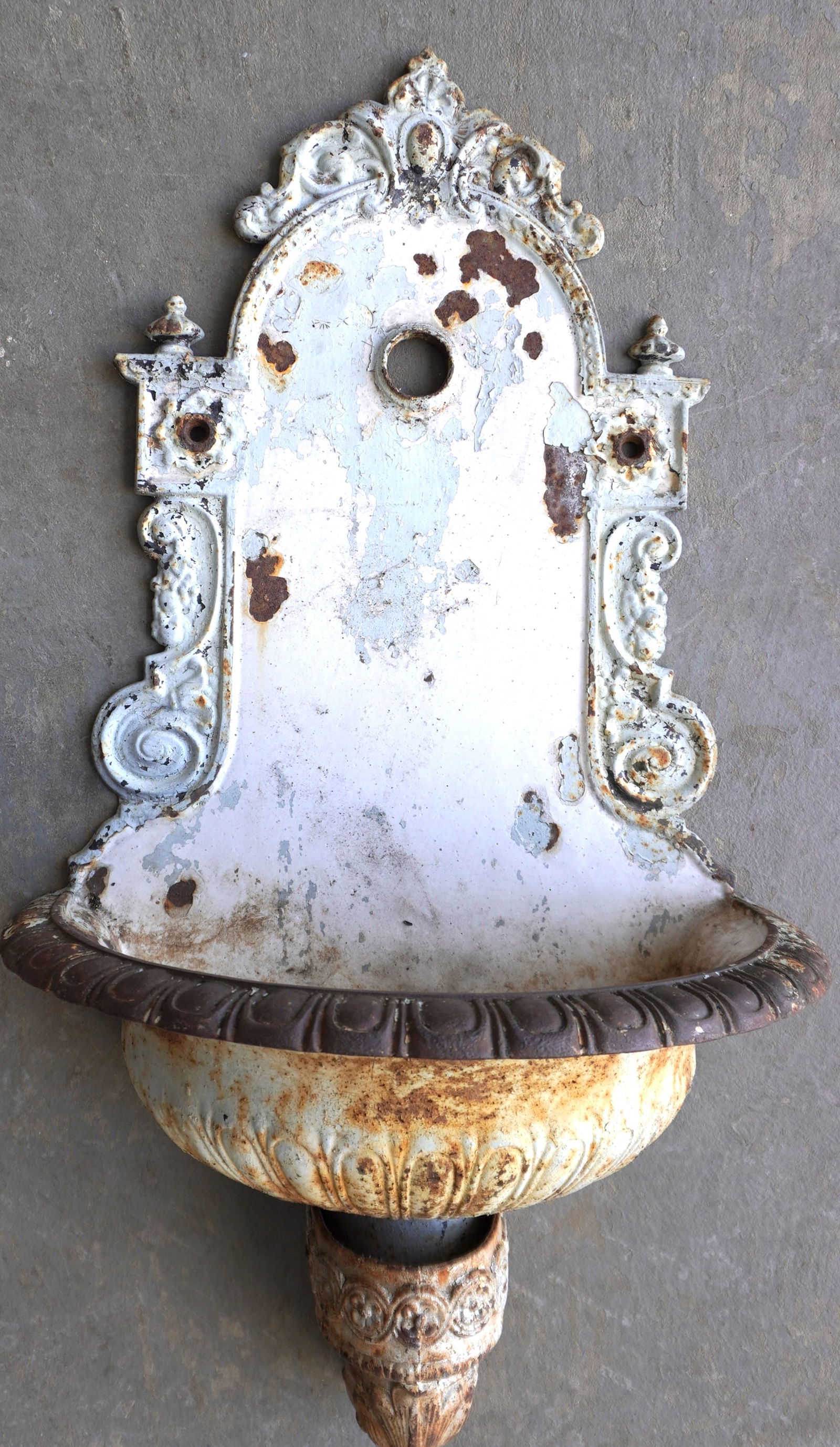 A cast iron wall mount water fountain in old worn white paint, probably last 19th to early 20th: A cast iron wall mount water fountain in old worn white paint, probably last 19th to early 20th century. Missing fountain hardware, some surface rust, but overall good condition. Measures 20"W x 11 1/