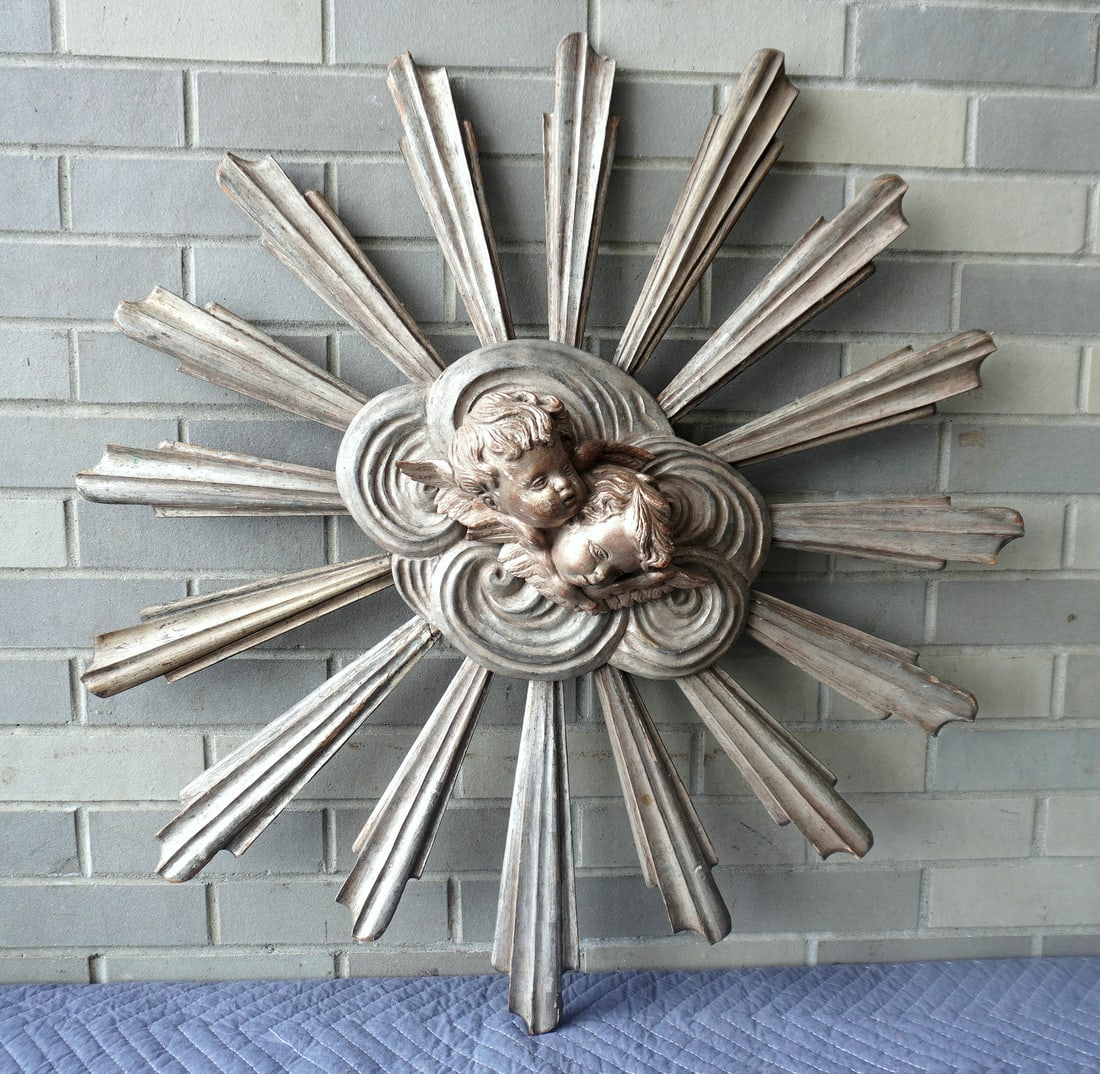 An Italian sculpture of a sunburst having hand carved figures of 2 cupids mounted in the center.: An Italian sculpture of a sunburst having hand carved figures of 2 cupids mounted in the center. Worn silver & gold paint, one of the rays repaired, overall good condition and signed "Made in Italy" o