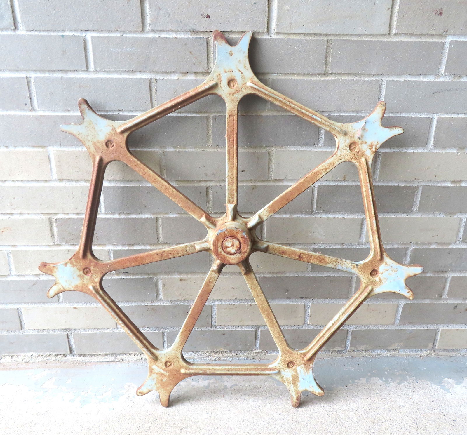 An architectural heavy cast iron gear with spiked perimeter, late 19th century with traces of: An architectural heavy cast iron gear with spiked perimeter, late 19th century with traces of original gray paint - measures 28 1/4" diameter x 2 3/4" thick. Some surface rust and the axel has broken