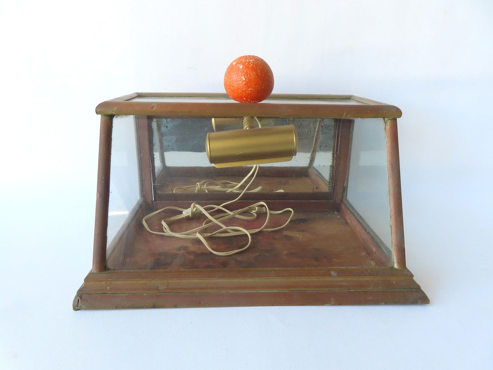 A small table top country store showcase with slanted front, drop down back door with interior: A small table top country store showcase with slanted front, drop down back door with interior mirror, copper frame with molded stepped base, and later adapted lighting device on interior which is eas