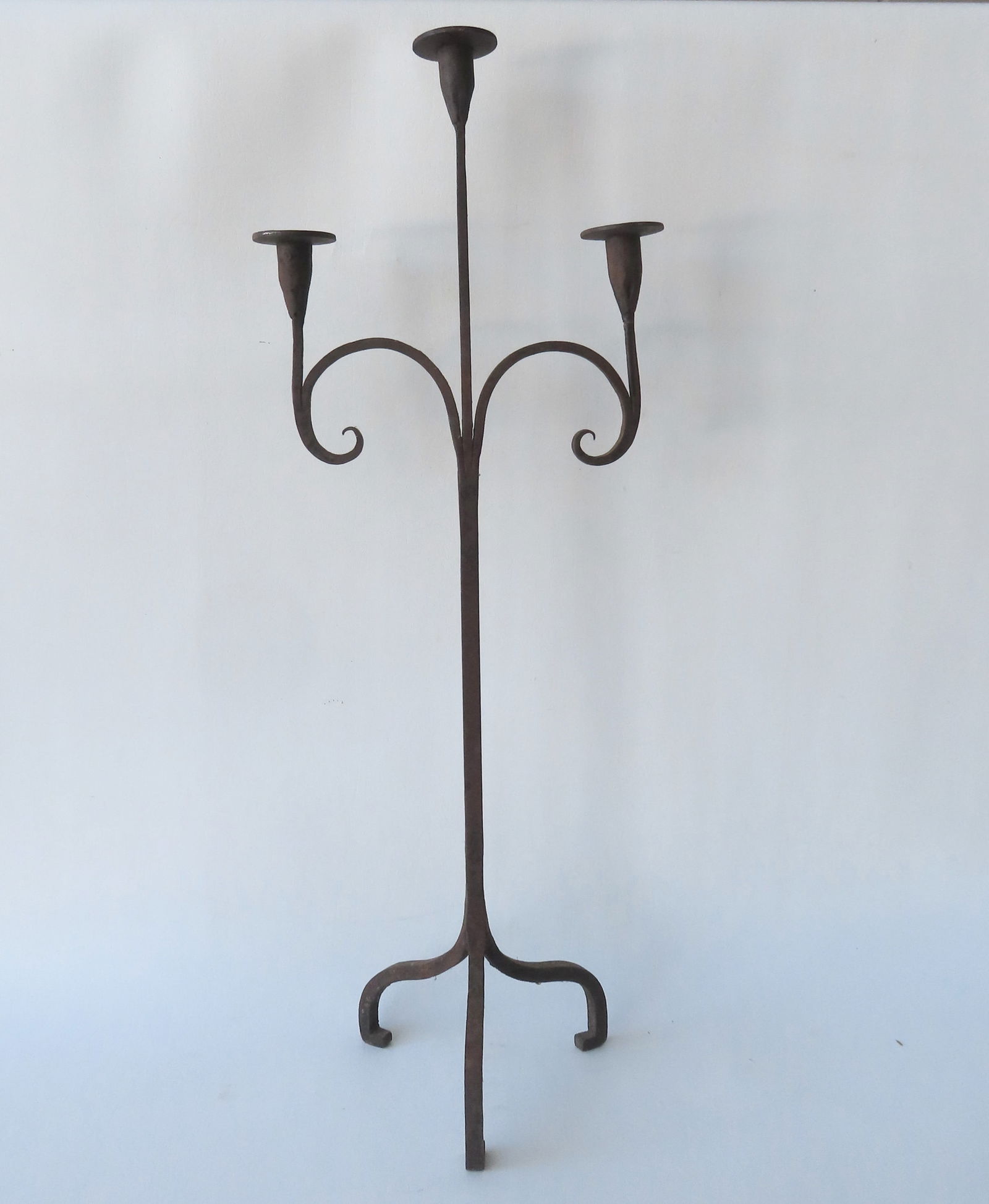 A hand forged iron floor standing candelabra with 3 candle holders supported by scrolled arms. The (1 of 6)