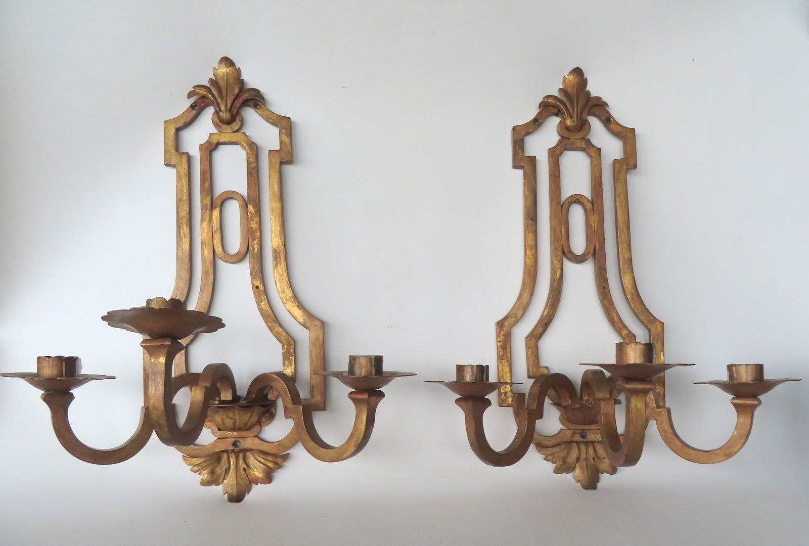 A pair of Arts & Craft style gilded cast iron and tin, wall mounted candelabras with 3 scrolled arms: A pair of Arts & Craft style gilded cast iron and tin, wall mounted candelabras with 3 scrolled arms holding candle fonts, and having a pierced work design in back plate, and with attached gilded tin