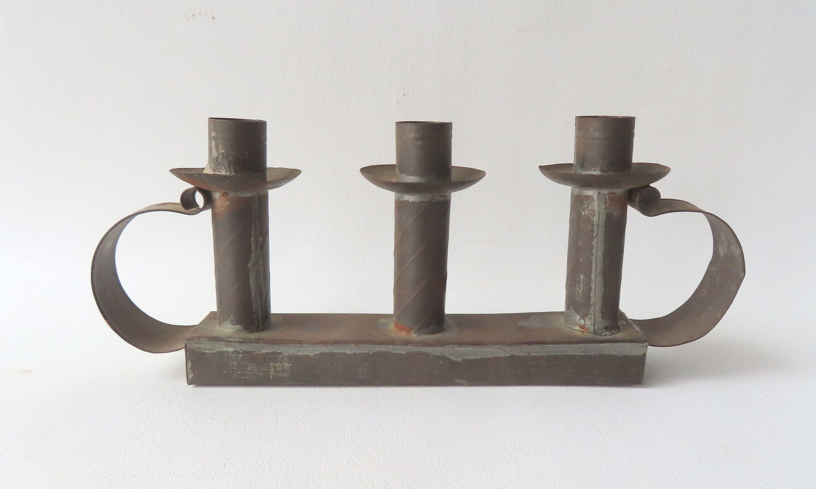 An early tin candle lighting device with 3 lights with drip pans, mounted on a rectangular base and: An early tin candle lighting device with 3 lights with drip pans, mounted on a rectangular base and having double scrolled handles, late 18th to early 19th century. Good condition. Measures 11 1/2"L x