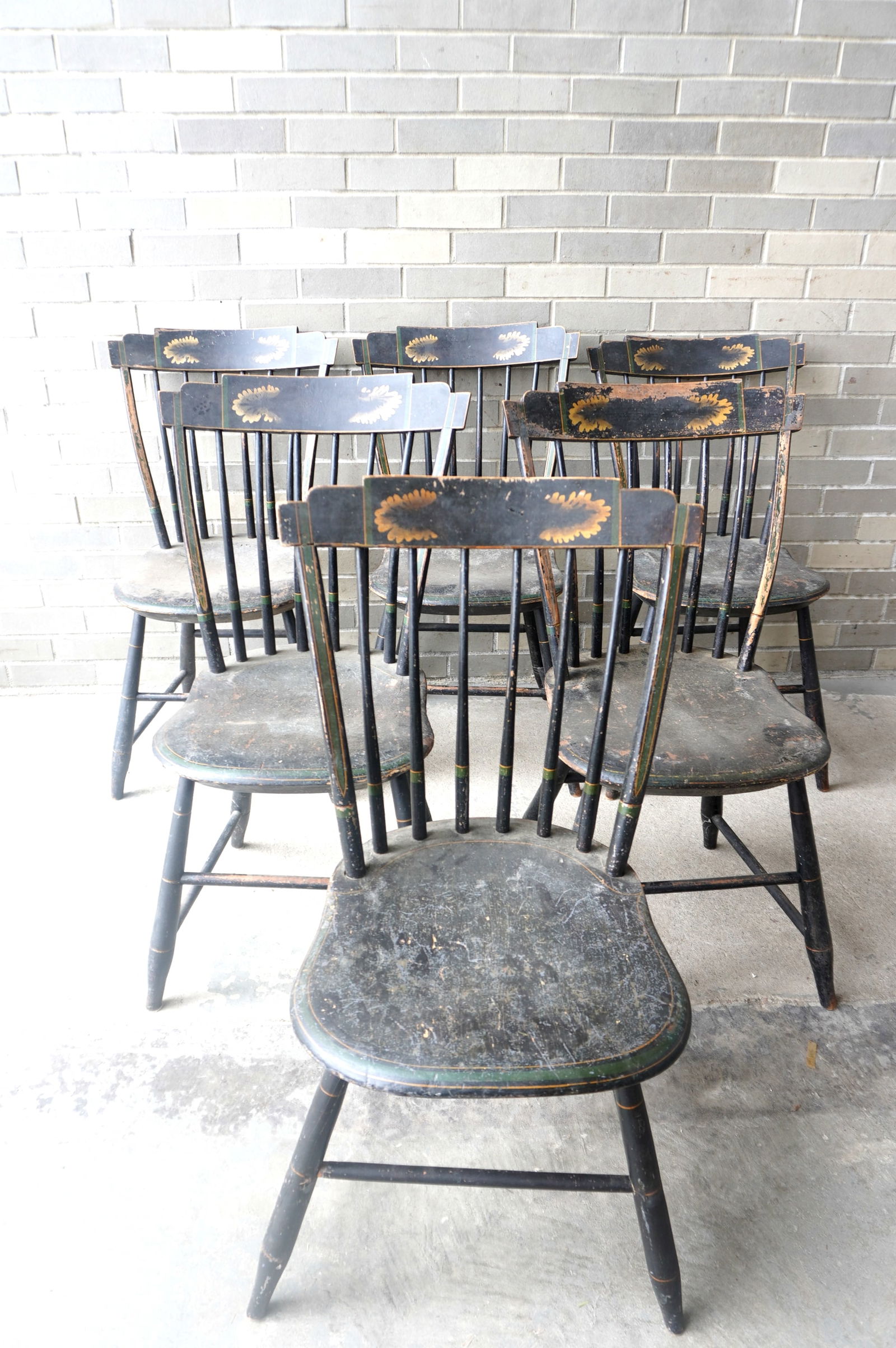 A set of 6 matching hand painted step-down Windsor chairs, with saddle seats, the crest decorated: A set of 6 matching hand painted step-down Windsor chairs, with saddle seats, the crest decorated with stenciled leaves over black ground with yellow pin striping throughout, circa 1800. The paint is