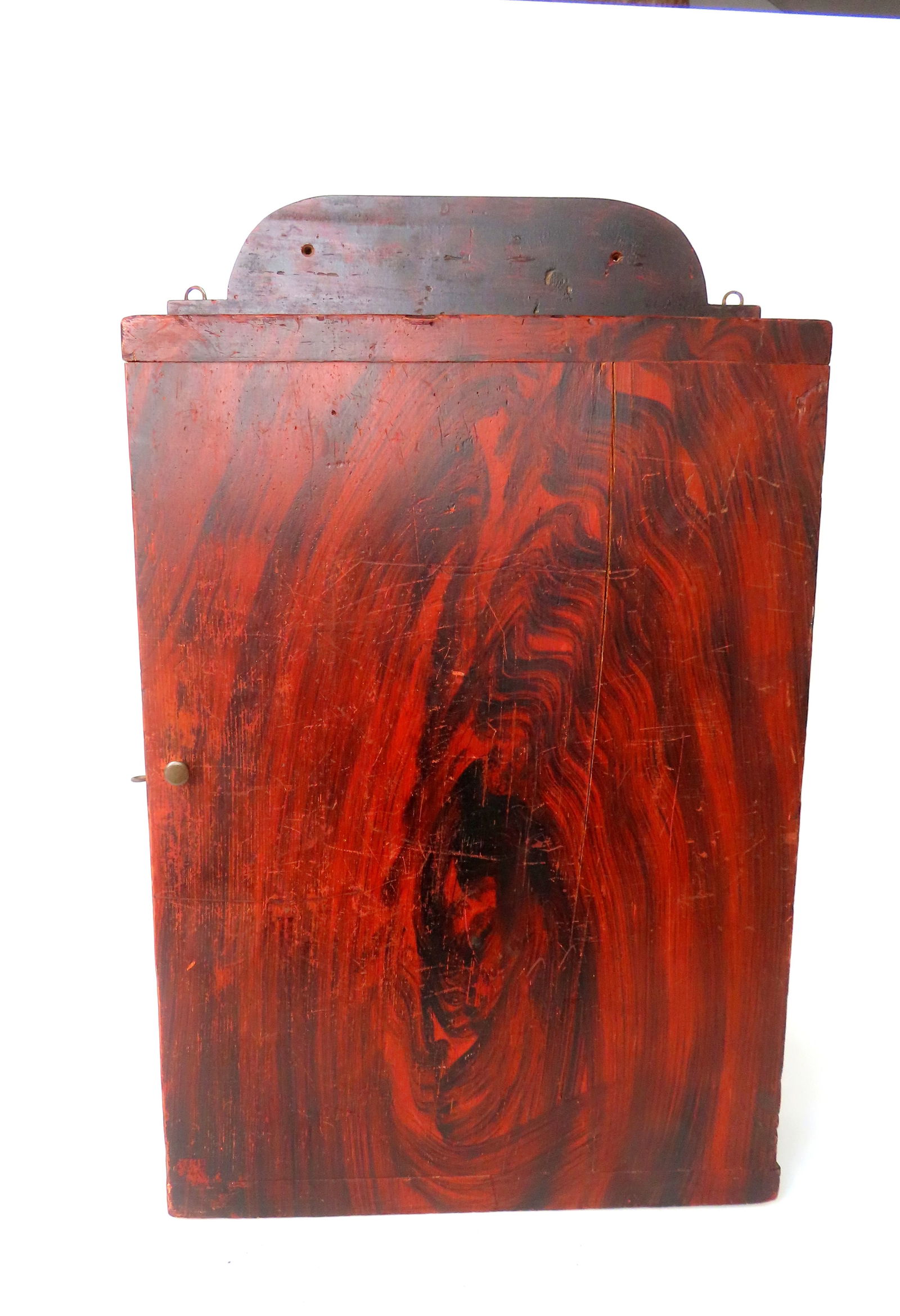 A good country grain painted wall hanging shelf with single door and rounded crest, probably New: A good country grain painted wall hanging shelf with single door and rounded crest, probably New England, early to mid 19th century. Square nail construction and having a 2 board hand planed back. All