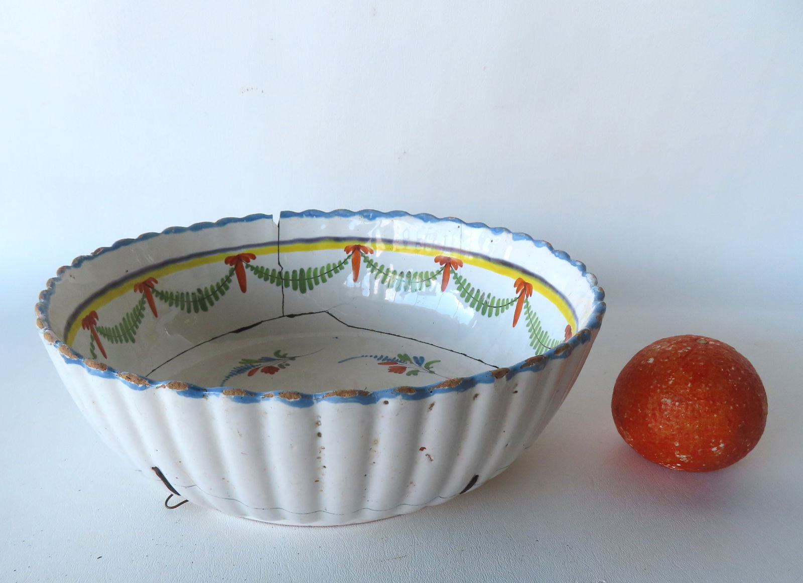 A large early tin glazed ribbed earthenware bowl decorated with swags and flowers, probably: A large early tin glazed ribbed earthenware bowl decorated with swags and flowers, probably Delftware, 18th century. Cracks repaired with staples (one staple is missing), and minor use wear to the gla