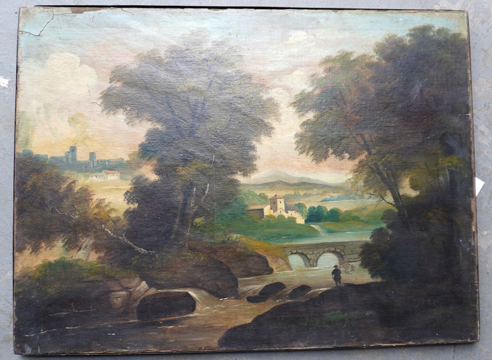 A primitive mid 19th century landscape depicting man fishing in stream near arched stone bridge with: A primitive mid 19th century landscape depicting man fishing in stream near arched stone bridge with buildings in background. Relined, noticeable border repairs with paint touchups, else good conditio