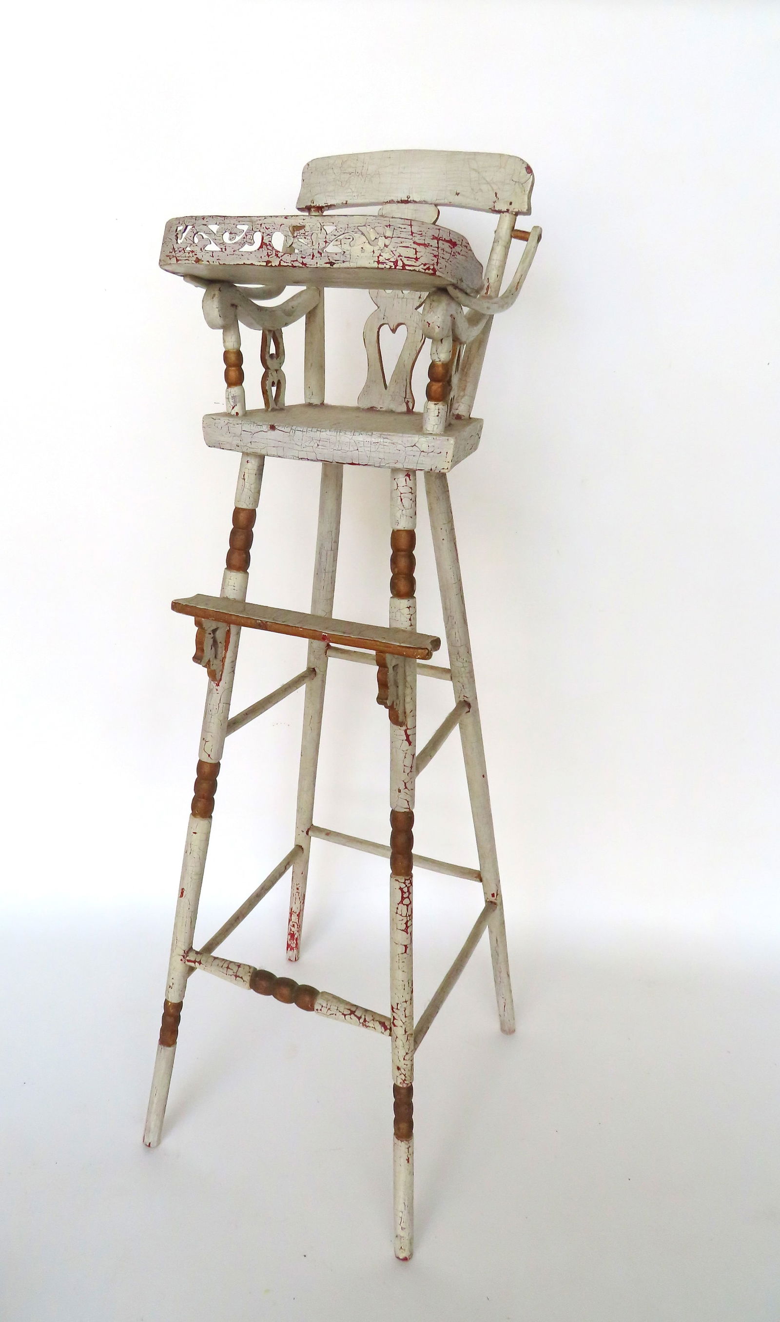 A doll's high chair in original white paint with gilded highlights on splayed legs, and having a: A doll's high chair in original white paint with gilded highlights on splayed legs, and having a back splat with 2 cutout hearts, and matching double hearts supporting the shaped arms, all hand made,