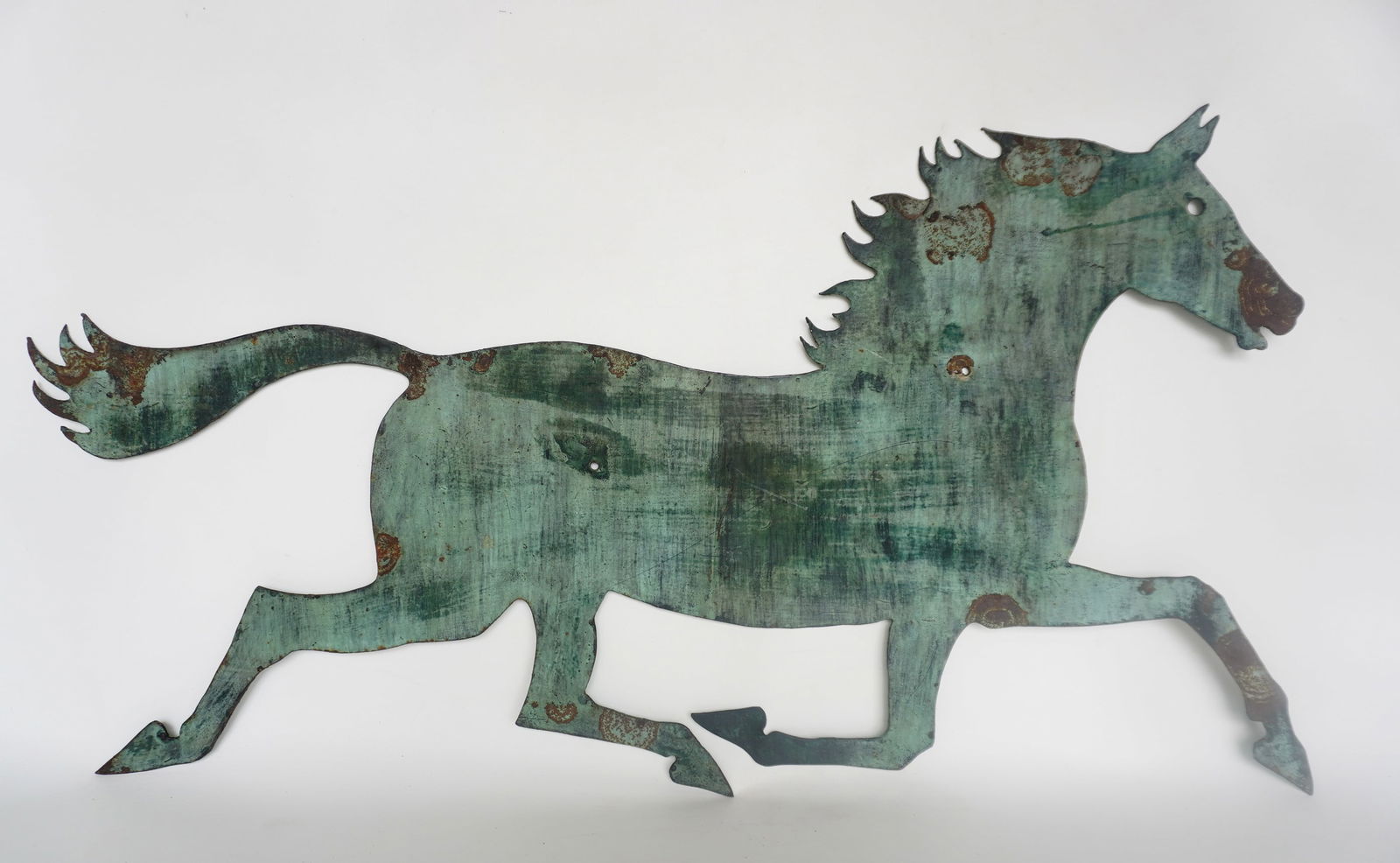 A folk art sheet iron trade store sign in the form of a running horse in old grey weathered paint,: A folk art sheet iron trade store sign in the form of a running horse in old grey weathered paint, likely for a blacksmith shop, circa 1850. Note the 2 holes in the body that were used to bolt it to a