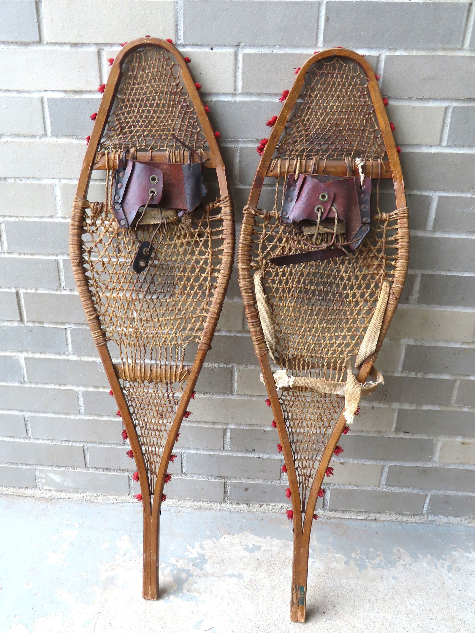 Pair of Native American snow shoes with original red yarn applied to the sides, probably late 19th: Pair of Native American snow shoes with original red yarn applied to the sides, probably late 19th to early 20th century. Each measures 36 5/8"L x 10 1/2"W. The leather straps/harnesses likely late ad