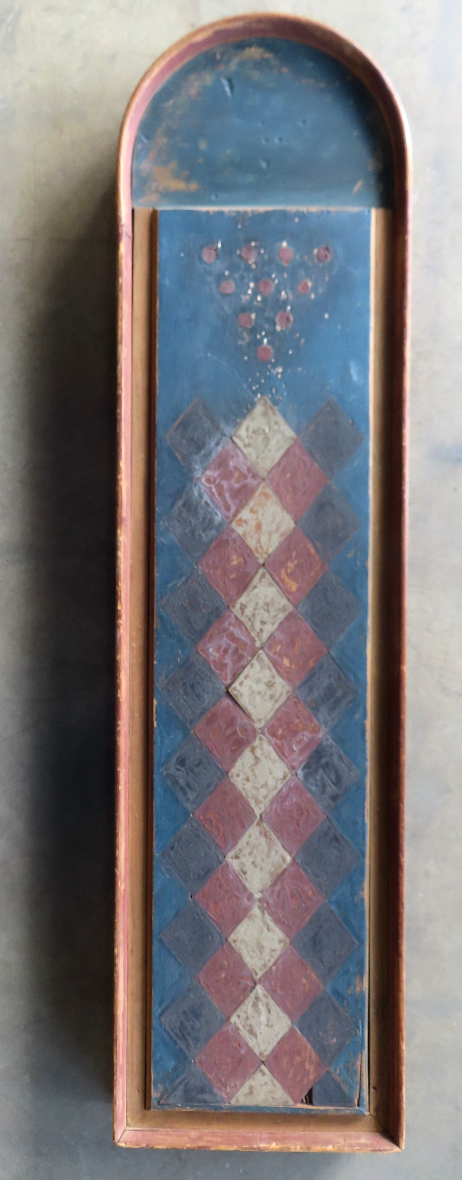 A large wooden architectural dome top game board, probably a 19th century bowling game. The front: A large wooden architectural dome top game board, probably a 19th century bowling game. The front surface decorated in a painted harlequin diamond pattern on a blue ground below a bowling pin form arr