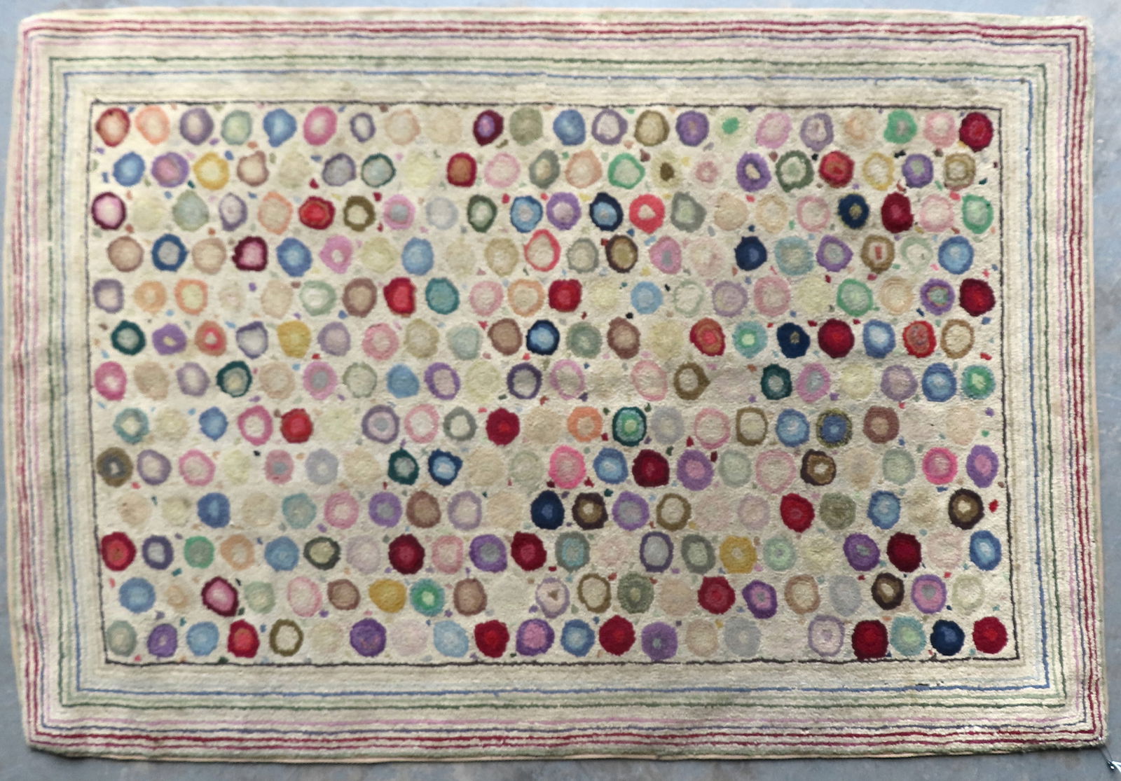 A Pearl McGowen design hooked rug titled on reverse border canvas "Cats Paw" signed Edna Johnson: A Pearl McGowen design hooked rug titled on reverse border canvas "Cats Paw" signed Edna Johnson (rug hooker) with small circular colorful "foot prints" surrounded by a concentric rectangular lines, p