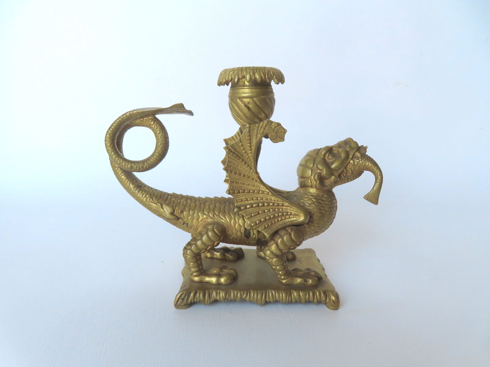 A polished bronze candle sconce in the form of a winged dragon swallowing fish attached to bronze: A polished bronze candle sconce in the form of a winged dragon swallowing fish attached to bronze footed base, very good condition, 19th century - measures 7 1/4"W x 5 1/4"H. Provenance: From the Marn