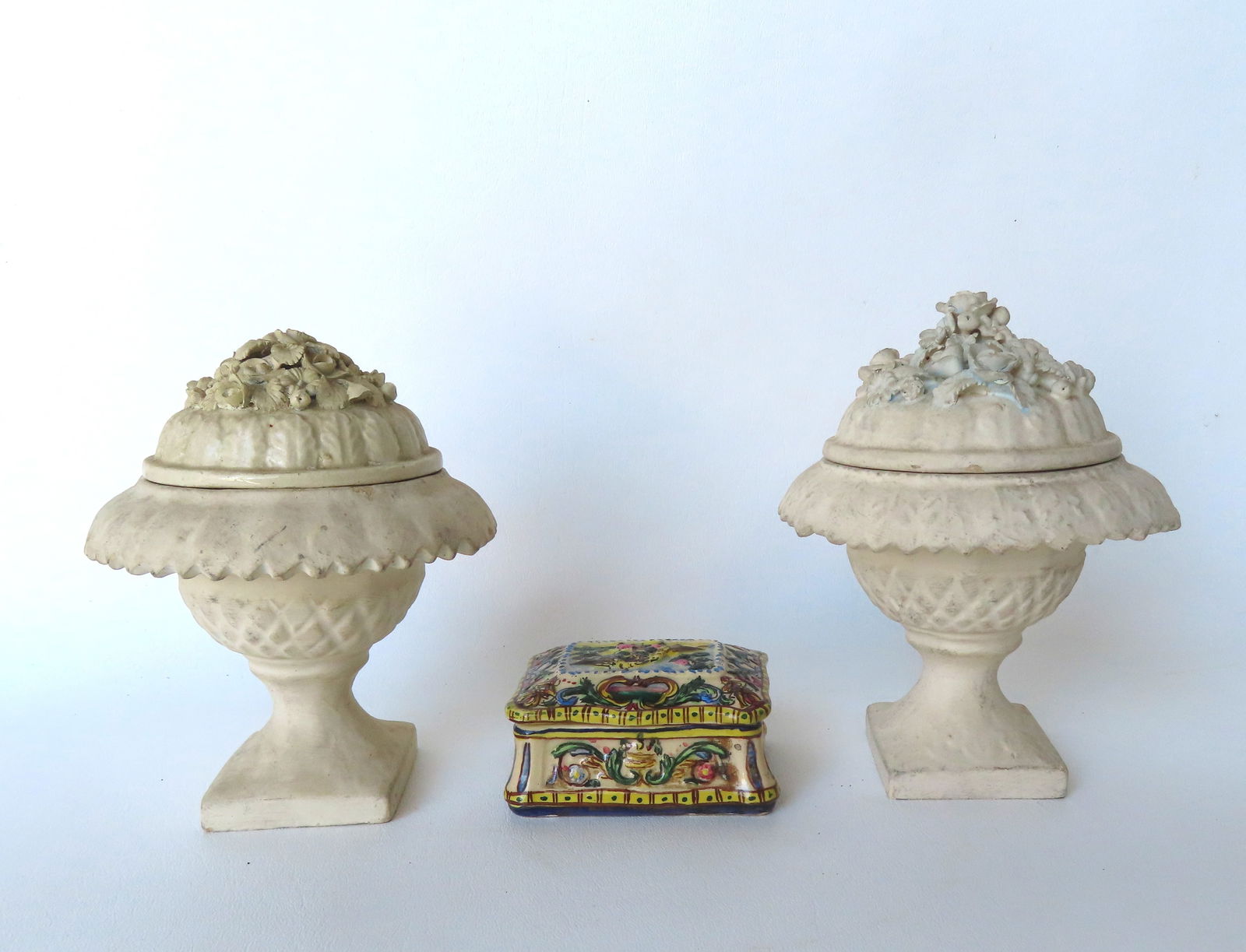 A pair of small covered matching earthenware urns, painted off-white similar to chalkware, with the: A pair of small covered matching earthenware urns, painted off-white similar to chalkware, with the mark of Bassano Nove Factory, Italy, 19th Century - both lids with floral and leaf finials, one lid