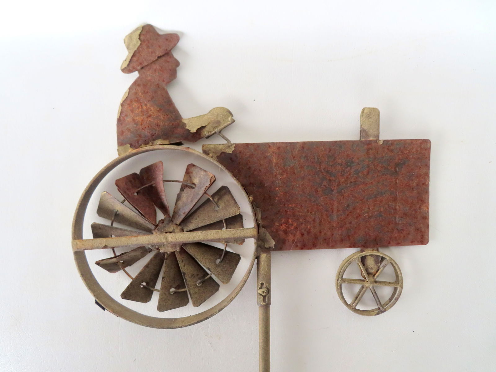 A tin whirligig lawn ornament in the form of a farmer driving tractor, mid to late 20th century. Tra: A tin whirligig lawn ornament in the form of a farmer driving tractor, mid to late 20th century. Traces of original paint, surface rusting, but overall good condition.