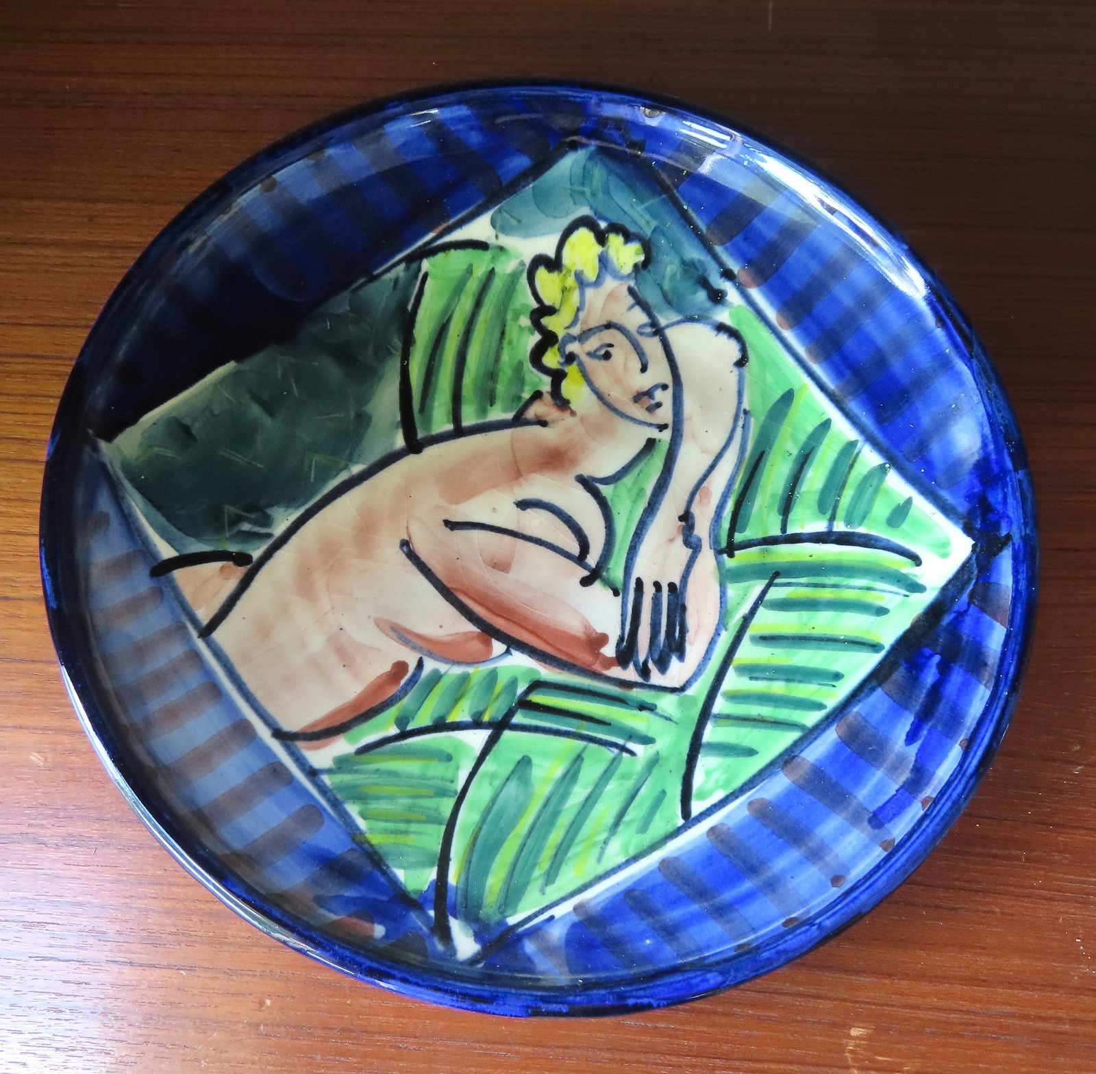 A colorful mid-century style terra cotta artistic plate, hand painted with the figure of a stylized: A colorful mid-century style terra cotta artistic plate, hand painted with the figure of a stylized nude lady resting on pillow, circa 1960-80 and in very good condition - measures 10 3/8" diameter. P