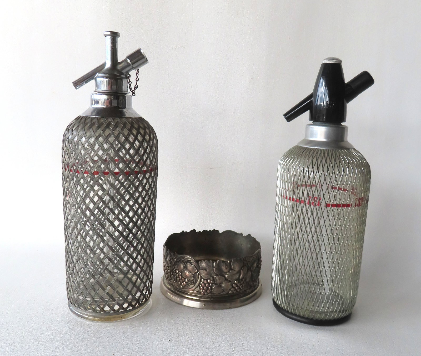 Two vintage selzter bottle dispensers, circa 1970, both with cross-hatch silver wiring over glass: Two vintage selzter bottle dispensers, circa 1970, both with cross-hatch silver wiring over glass cylinders. One with nickel plated works signed on base "Made in Czechlosvakia"; the other with black p