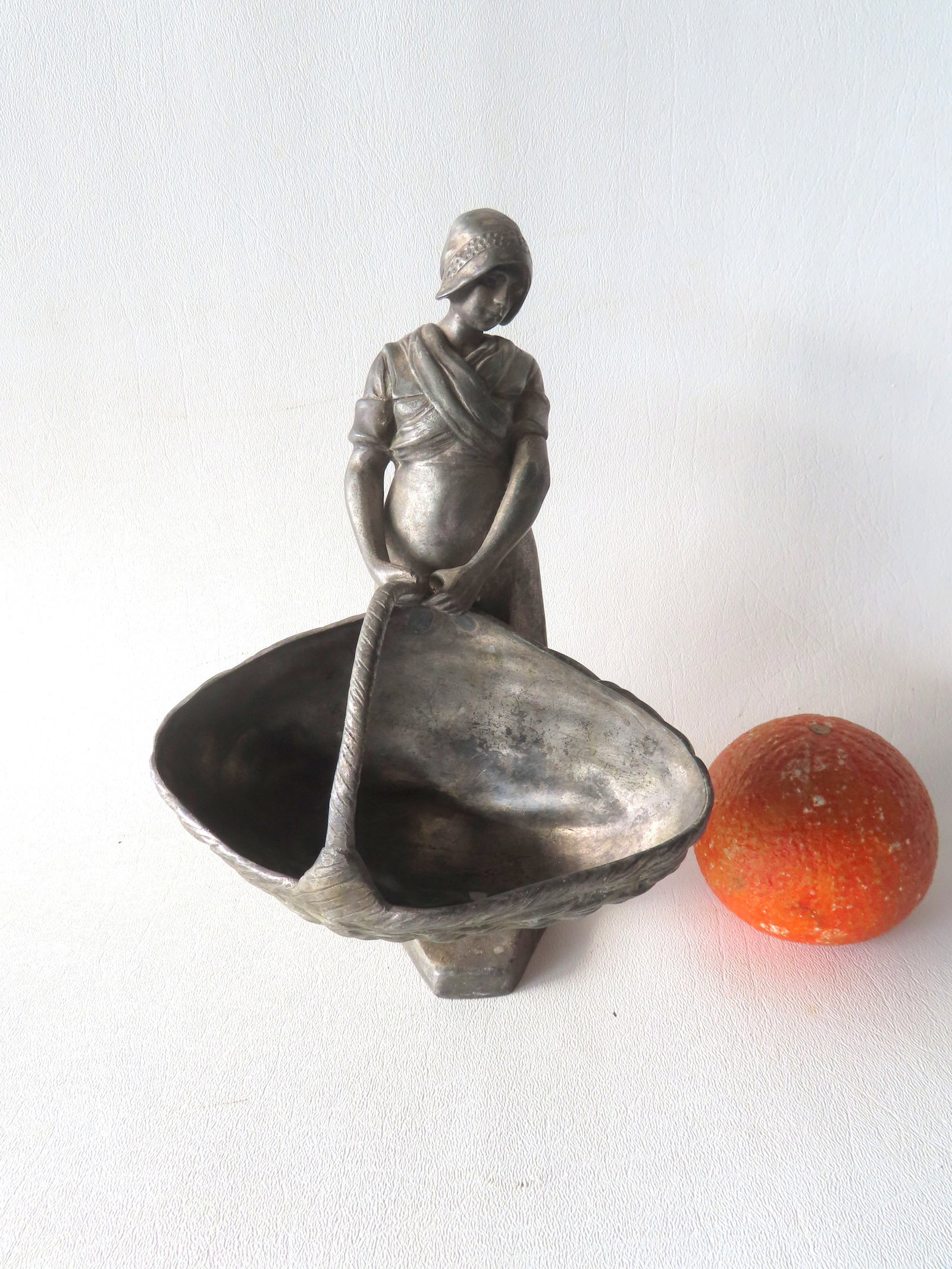 Metal sculpture of a Dutch lady holding a large basket, probably for holding flowers, late 19th: Metal sculpture of a Dutch lady holding a large basket, probably for holding flowers, late 19th century. Silver plated hollow-cast metal attached to solid metal base. Some wear to plating, otherwise g