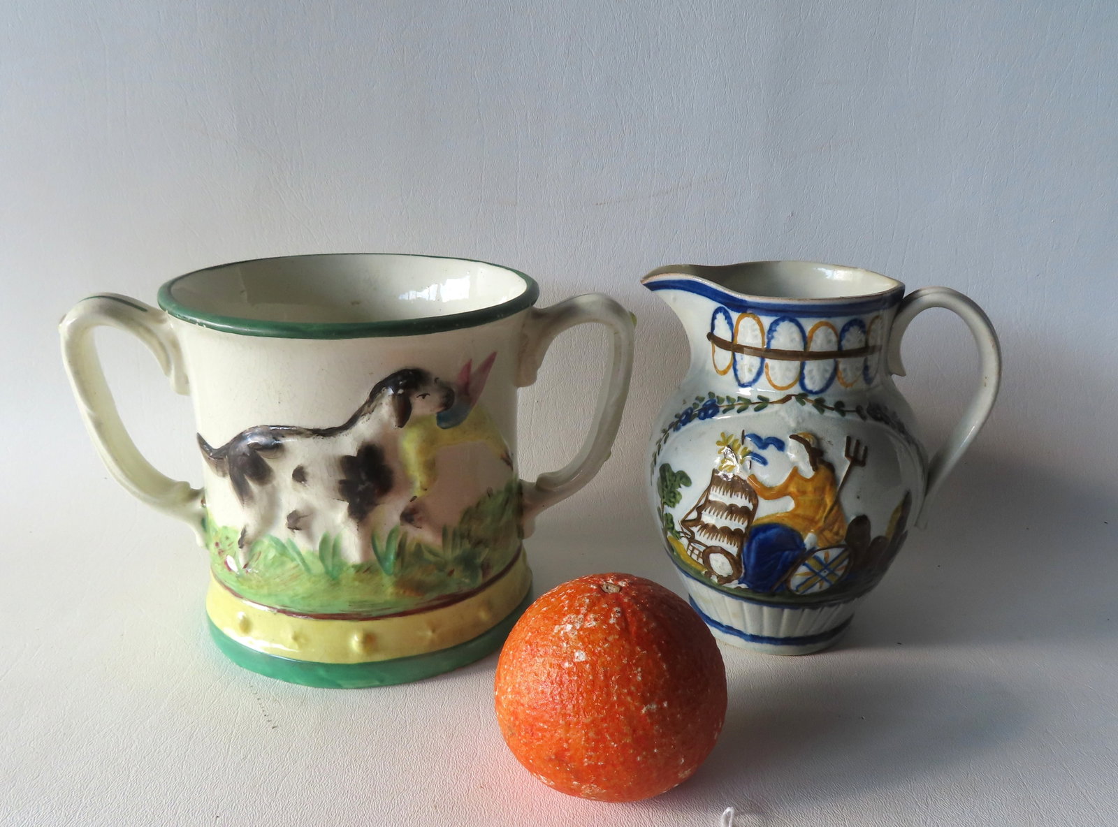 Two early English porcelain vessels. The first, a Staffordshire double handled frog mug, decorated: Two early English porcelain vessels. The first, a Staffordshire double handled frog mug, decorated with an embossed hand painted hunting dog with game bird in mouth on both sides of mug, and an applie