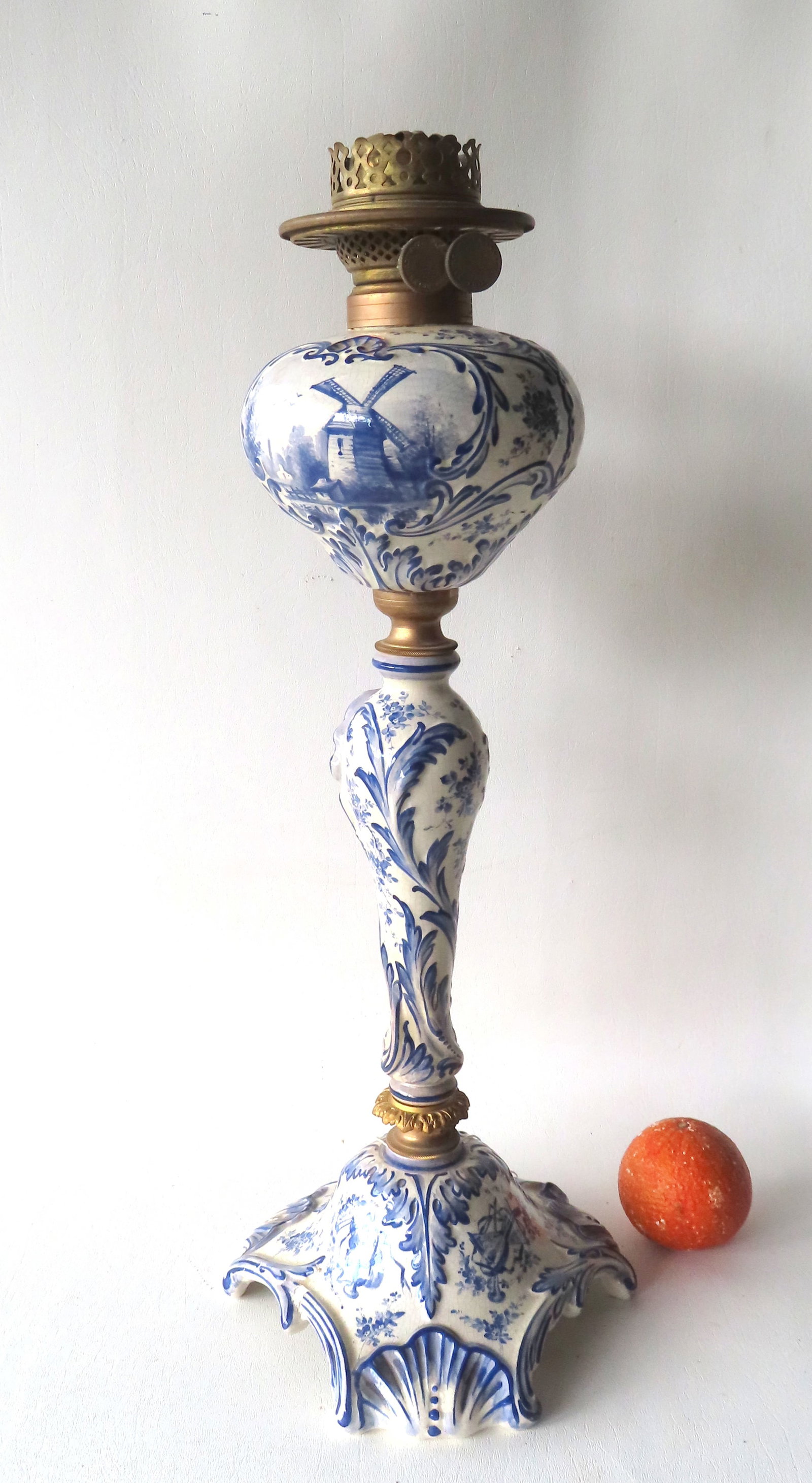 A large porcelain Delft style oil lamp with Crown over D hallmark on base - all hand painted with: A large porcelain Delft style oil lamp with Crown over D hallmark on base - all hand painted with Dutch scenes and embossed leaves and scrolls, circa 1870-90. The base with a repair to one foot, else 