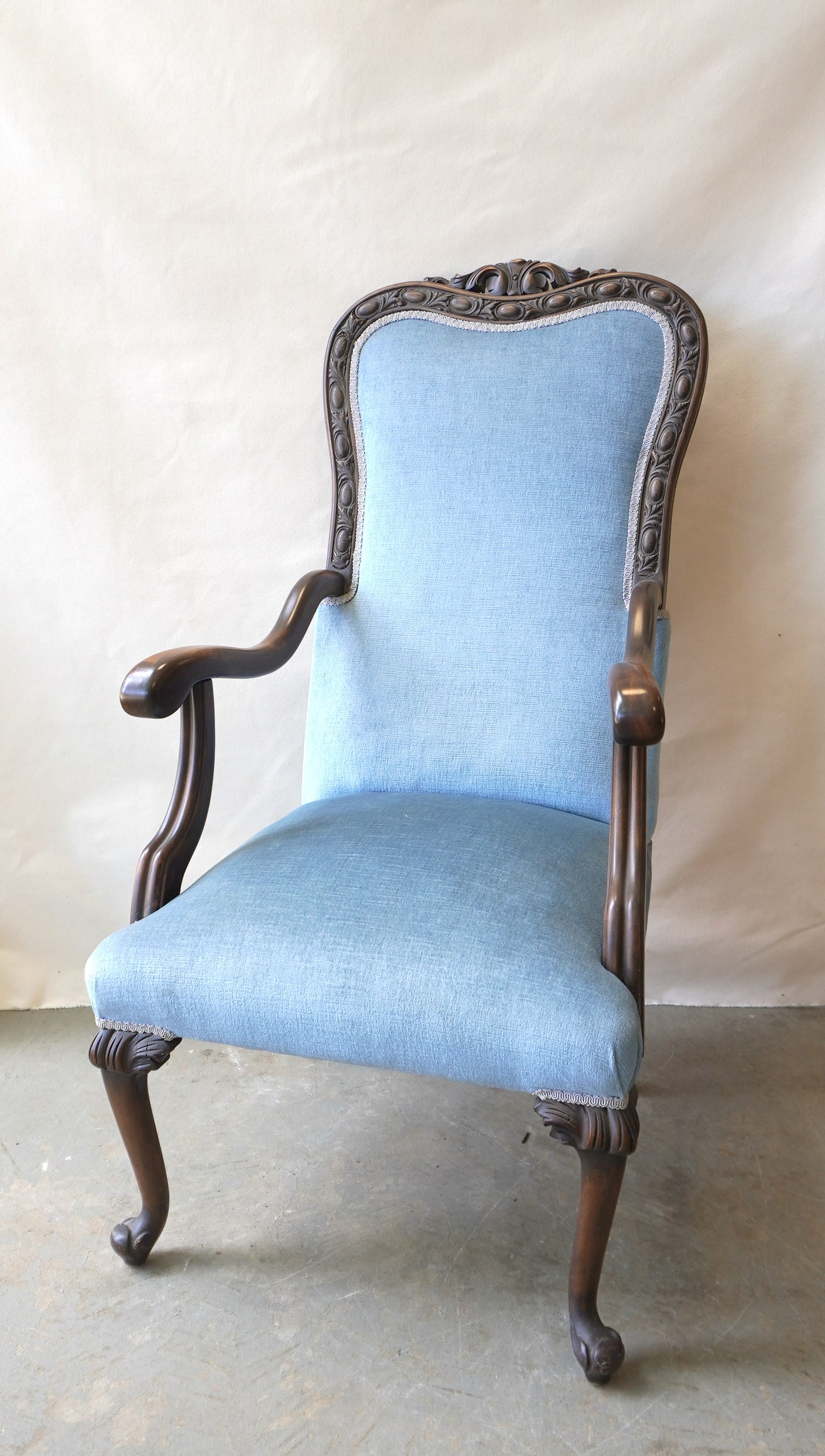 A Queen Ann style upholstered parlor chair having a high shaped back, with carved frame, scrolled: A Queen Ann style upholstered parlor chair having a high shaped back, with carved frame, scrolled arms and acanthus carved cabriole legs leading to carved pad feet, probably late 20th century in very 
