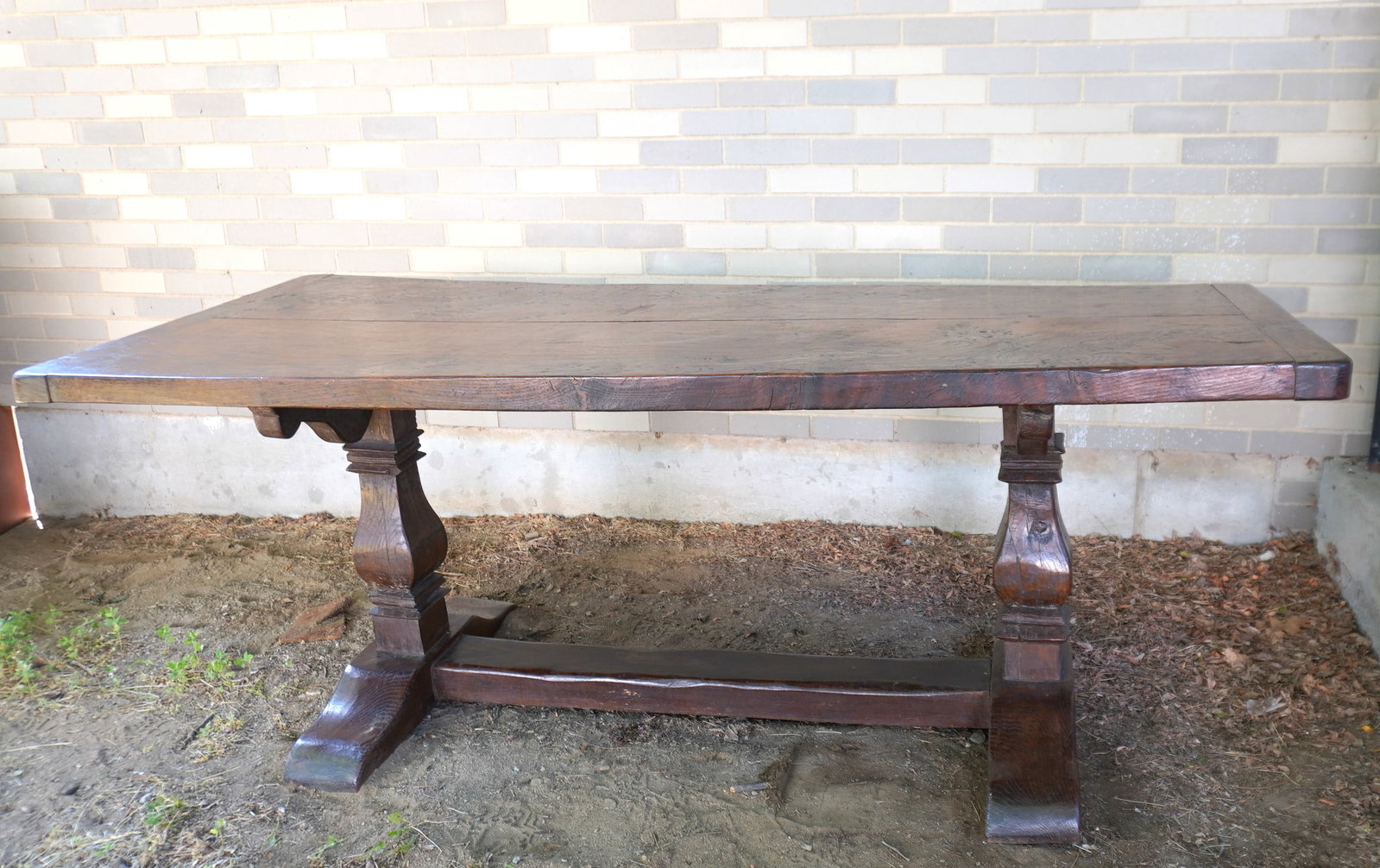 A primitive English elmwood trestle table. The thick top with breadboard ends mounted on 2 shaped: A primitive English elmwood trestle table. The thick top with breadboard ends mounted on 2 shaped columns and heavy stepped feet. Measures 78"L x 33 1/2" x 29 1/2"H. Very good condition, probably late