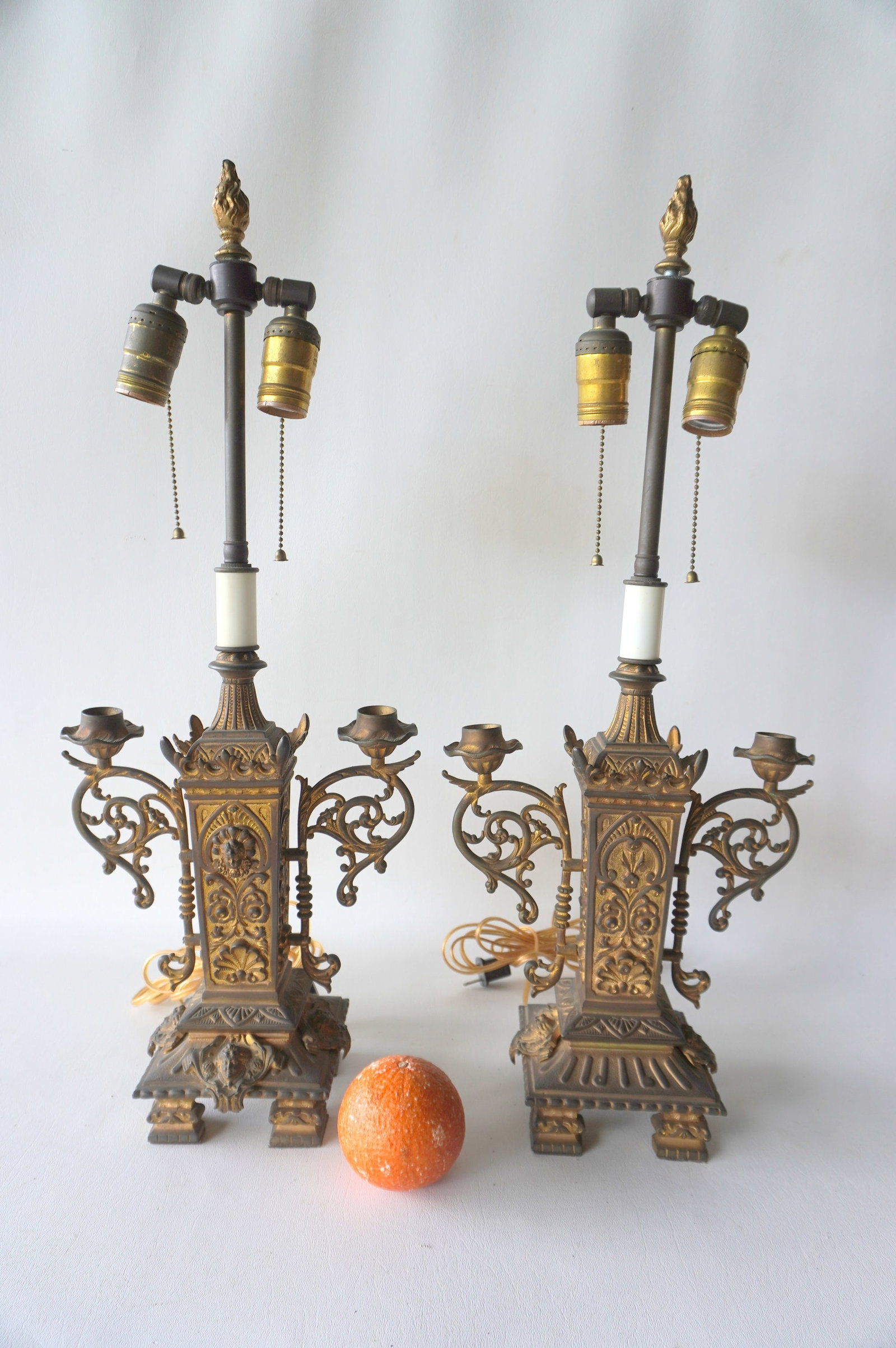 A pair of gilt bronze candleabras converted to table lamps with flame finials, probably French, 19th: A pair of gilt bronze candleabras converted to table lamps with flame finials, probably French, 19th century. Each with double fonts attached to ornate scrolled handles, below the added post that hold