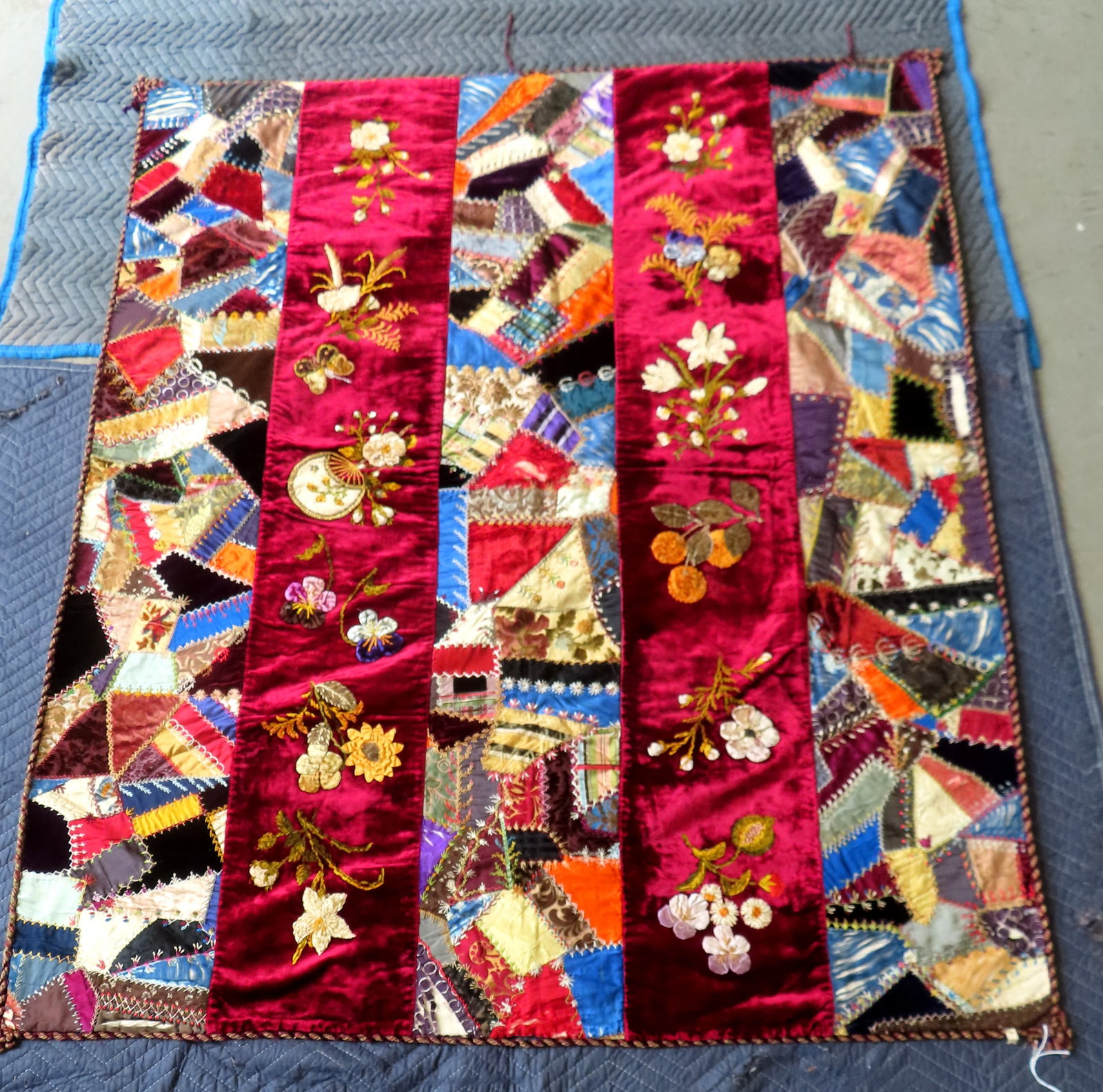 A beautiful crazy quilt decorated with 5 vertical panels of geometrics and flowers and having a: A beautiful crazy quilt decorated with 5 vertical panels of geometrics and flowers and having a braided border. Includes 2 panels decorated with embroidered stumpwork flowers and the 3 other panels wi