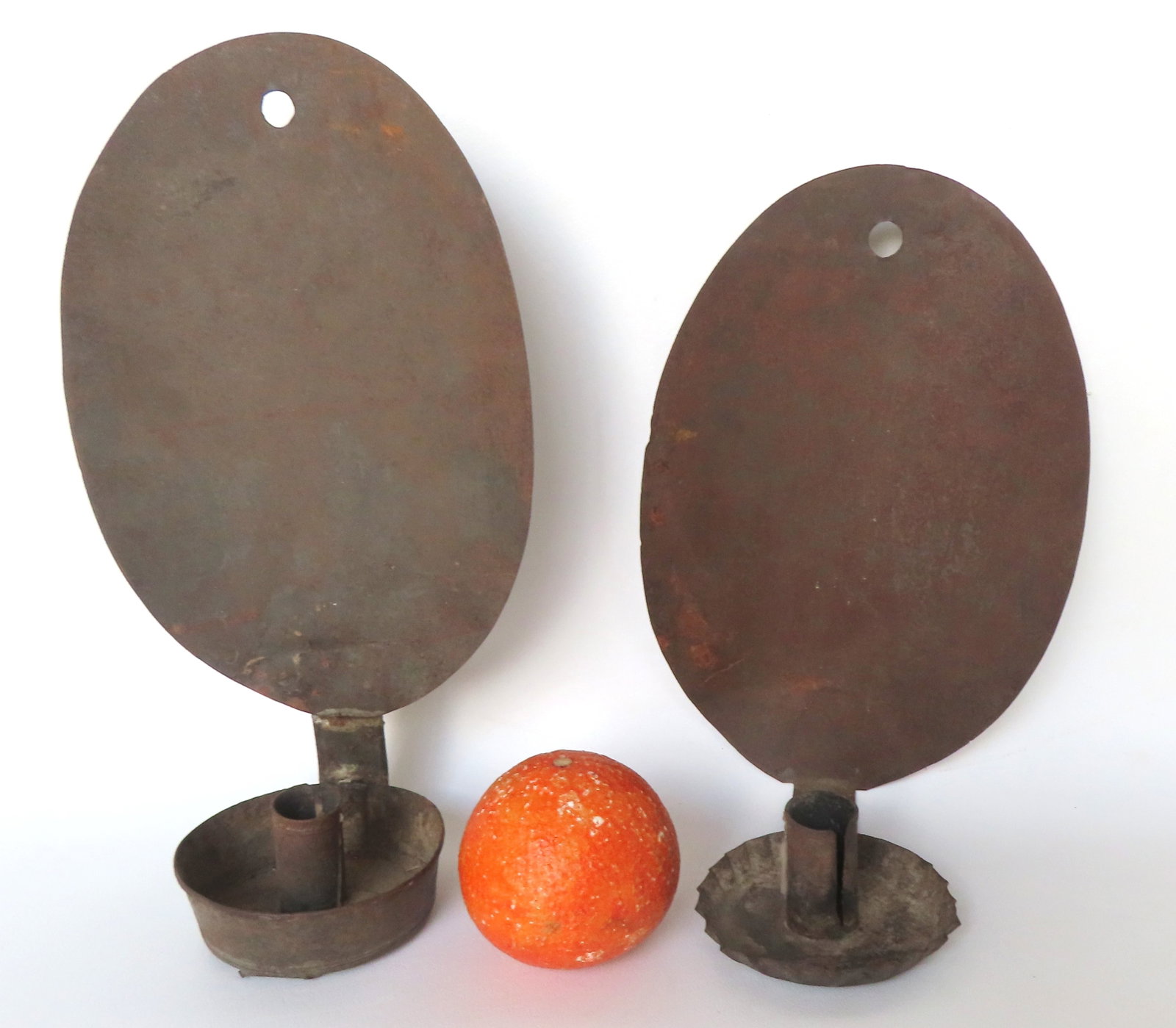 Two near matching tin candle wall sconces, with oval reflectors, both early to mid 19th century. One: Two near matching tin candle wall sconces, with oval reflectors, both early to mid 19th century. One with crimped drip pan 10"H x 6 5/8"W and the larger with a cup-shaped drip pan, 12 1/4" x 6 5/8"W. 