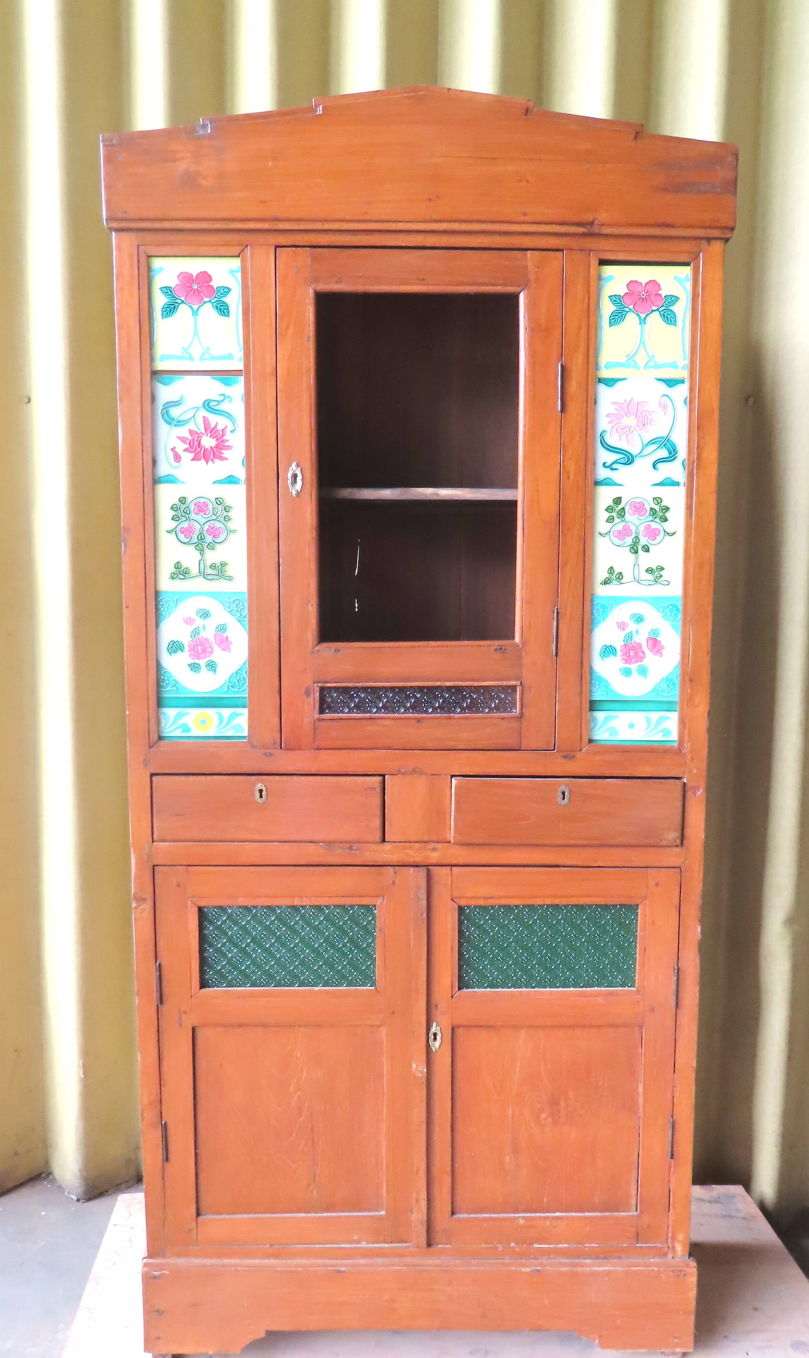 An Art Deco kitchen cabinet with porcelain tiles decorated with flowers, flanking both sides of the: An Art Deco kitchen cabinet with porcelain tiles decorated with flowers, flanking both sides of the central top door, over 2 drawers over 2 doors on cutout base with paneled sides, circa 1930. One of 