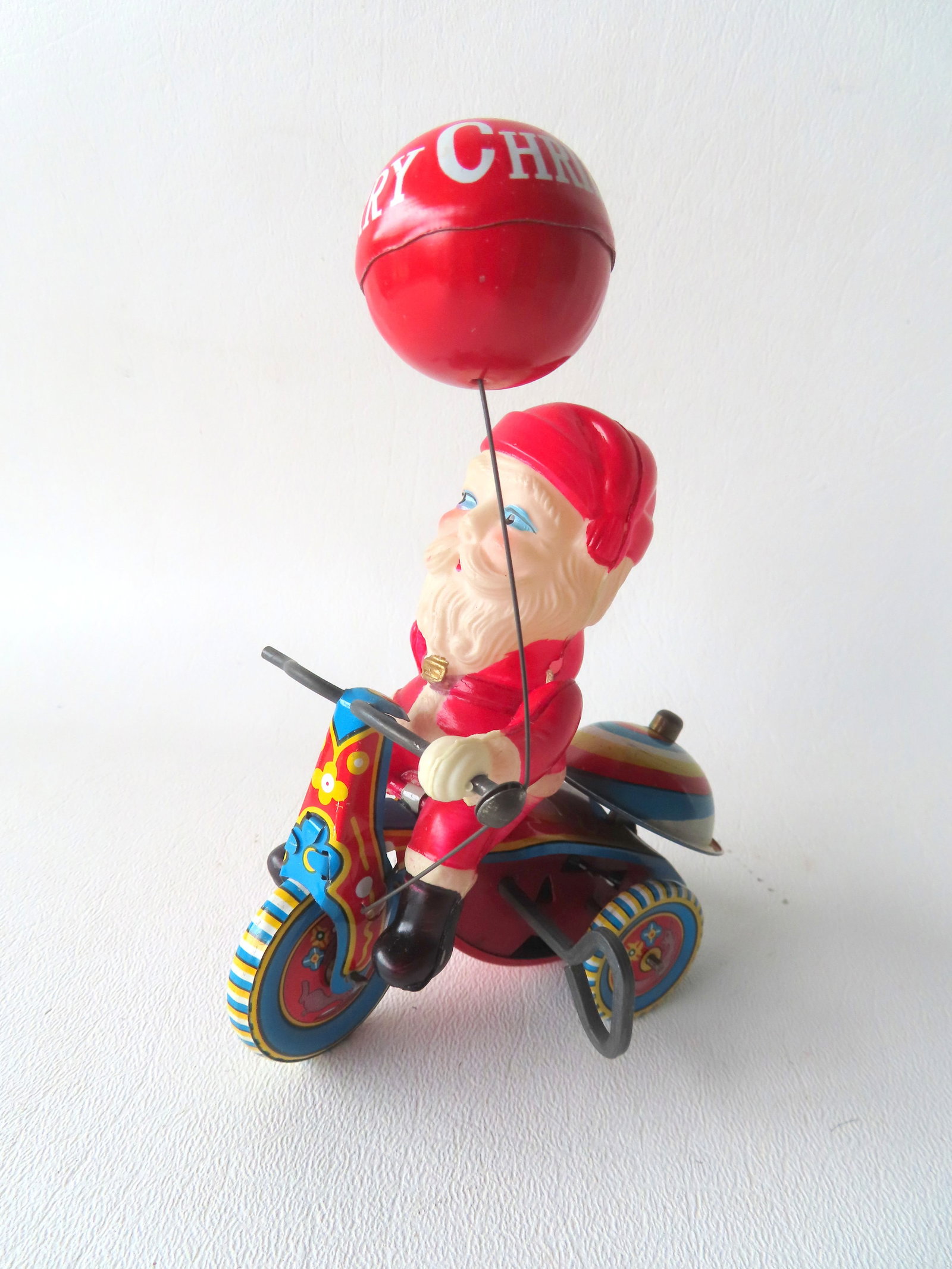 Celluloid and tin Japanese Santa Claus on tricycle with "Merry Christmas" balloon, signed "Suzuki / (1 of 4)