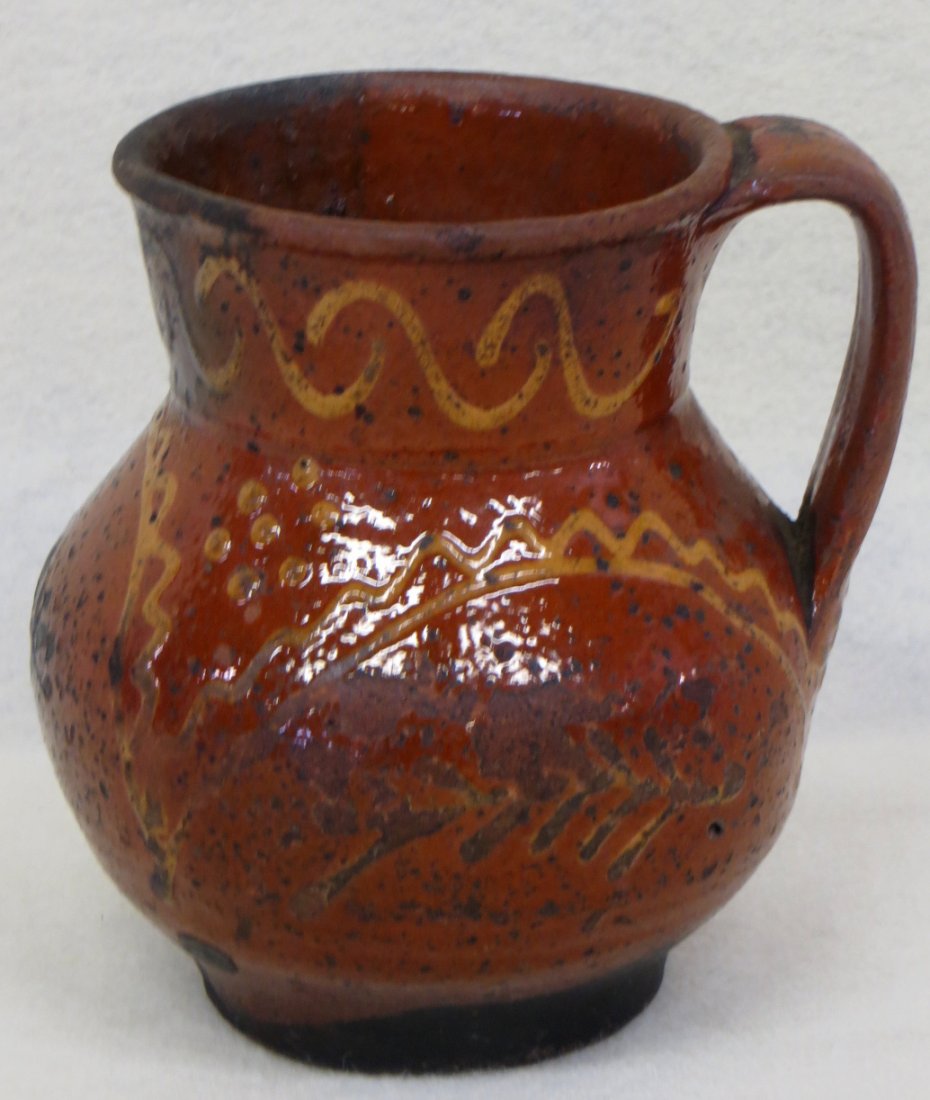 Redware pitcher with yellow slip decoration - 5.5"H. Sl: Redware pitcher with yellow slip decoration - 5.5"H. Slight glazing chips to rim, otherwise good overall condition.