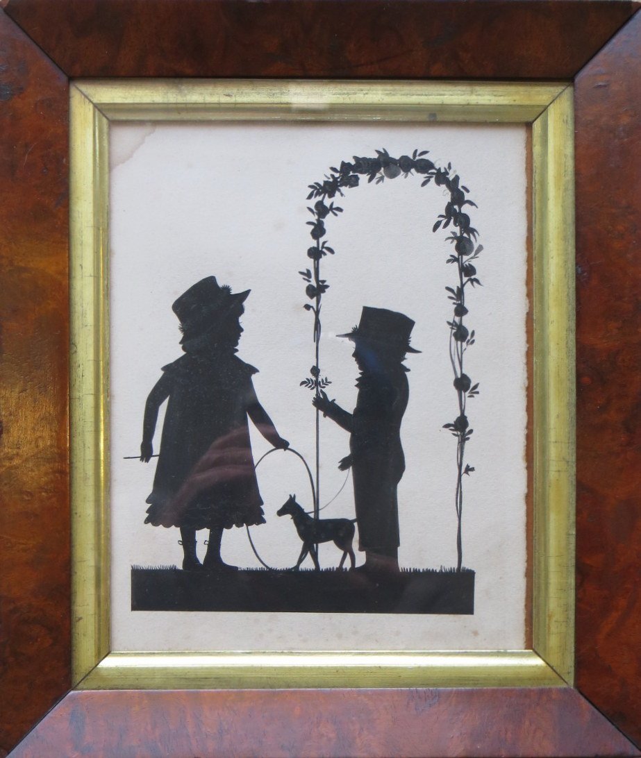 Early W/C silhouette of a young boy holding dog on: Early W/C silhouette of a young boy holding dog on leash standing under arbor near young girl with hoop and stick. Original burl wood frame with gold leaf inset. Mid-19th century. 6" x 7.25"