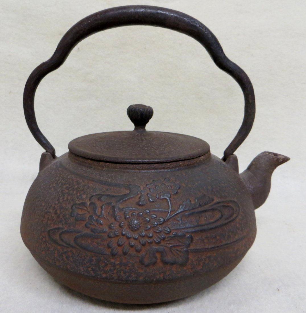 Cast iron textured tea kettle with floral decorations: Cast iron textured tea kettle with floral decorations on the sides with a flower bud finial at lid, signed under spout - overall height 7.5 inches to top of wrought iron handle Overall condition very 