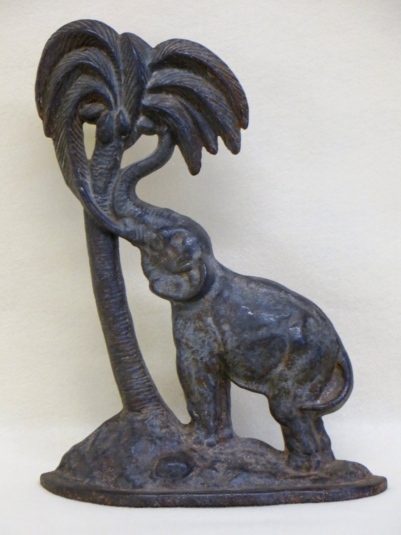 Cast iron door stop Elephant reaching for coconut in: Cast iron door stop Elephant reaching for coconut in palm tree - 13.5"H. Original paint with wear.
