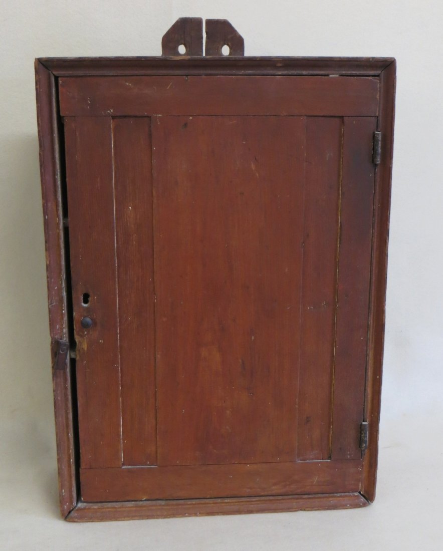 Old single door with raised panel wall cupboard in old: Old single door with raised panel wall cupboard in old red stain - 19th century - 16.5"W x 23"H x 6.5"D. Shrinkage split in back board, otherwise very good condition.