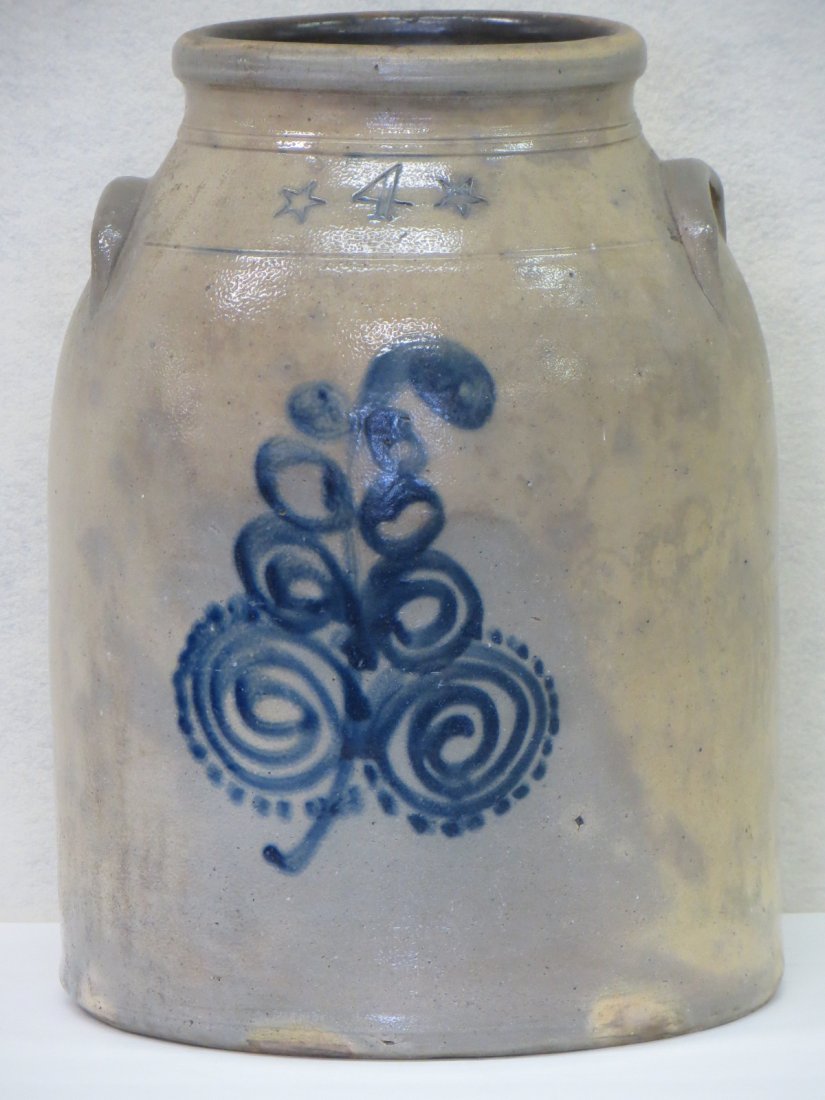 Four gallon stoneware jar with a cobalt watch spring &: Four gallon stoneware jar with a cobalt watch spring & flower design with two stamped stars bordering the stamped 4 (gal.). The jug has a tooled shoulder and neck and applied lug handles 14.75" H
