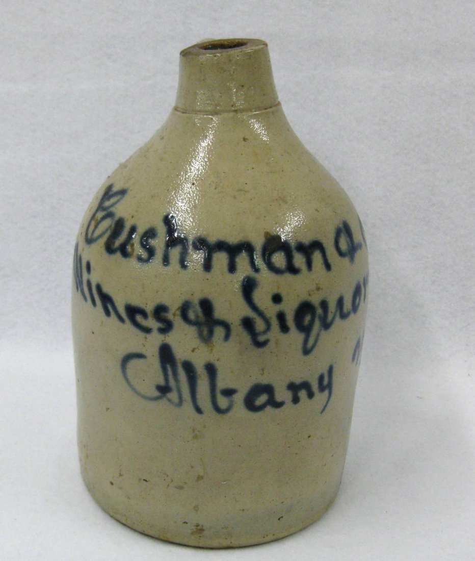 Stoneware advertising jug signed in blue script: Stoneware advertising jug signed in blue script "Cushman & Co. Wines & Liquors Albany NY". Several small rim chips, 1" hair line extending from base, otherwise very good condition. Provenance: The Van