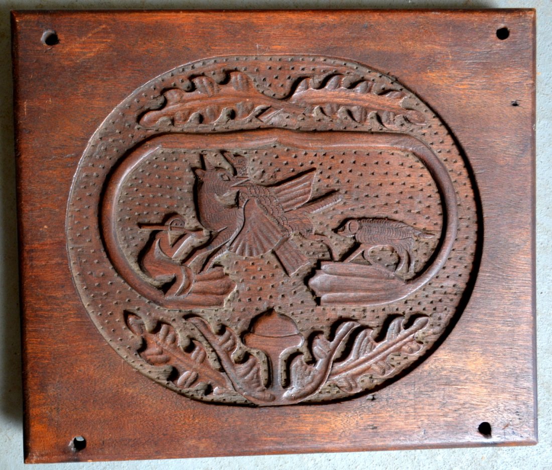 Folkart hand carved black walnut plaque depicting a: Folkart hand carved black walnut plaque depicting a hunter, fox with game, hunting dog and acorn and leaf border - 10.5" x 12.25". Four screw holes in each corner where it was mounted, else very good 