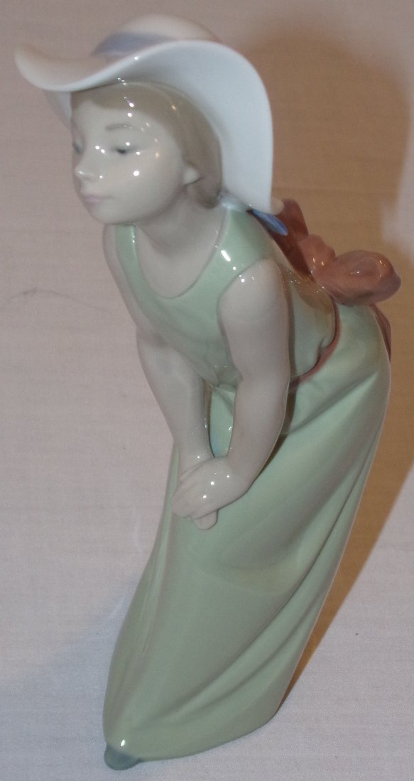 Lladro Figure: Lladro porcelain figurine, young lady in long pale green dress w/brown bow, leaning on her knees, incised, approx. 9” T
