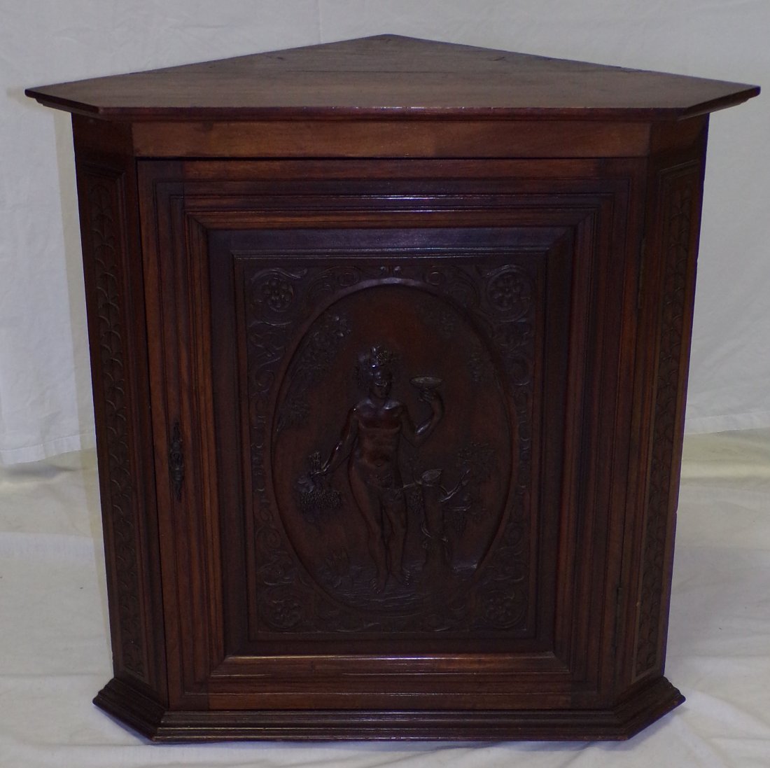 19th C European Corner Cabinet: 19th Century European walnut corner cabinet having a molded cornice over a blind door with center carved panel, raised design with a nude holding a cup with bunches of grapes, carved rosette corners, 