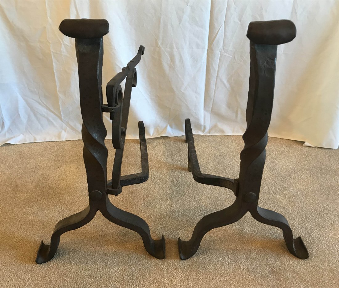 FURNITURE, ACCESSORIES, COUNTRY COLLECTIBLES, TOYS,: Pair of vintage Arts & Crafts style fireplace andirons, “chipped” design with scrolled tops on twisted columns, ending on scrolled feet, 1 iron has a swinging pot holder, each 23 ¾” T x 13 ½��