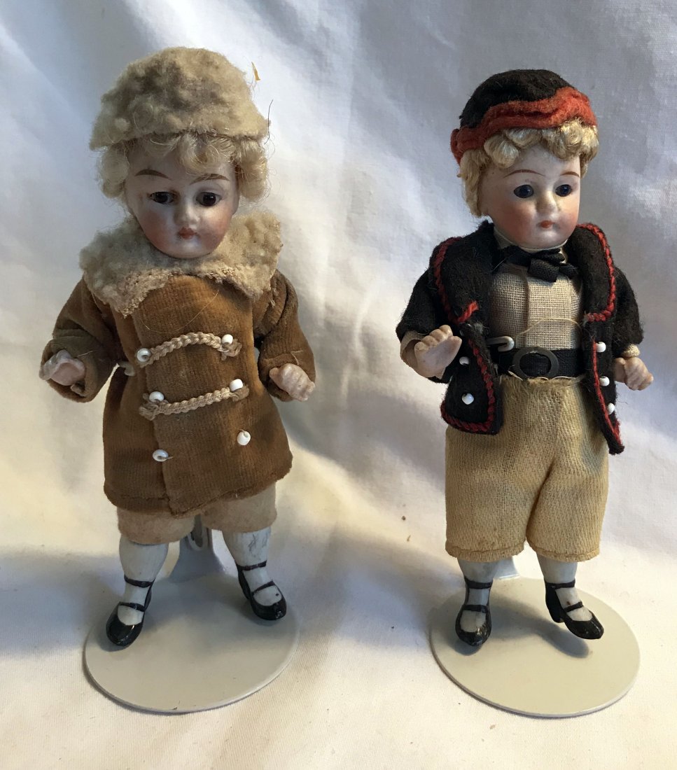 DOLLHOUSE, DOLLS, MINIATURES: 2 porcelain miniature dolls both with movable arms and legs, glass eyes: boy dressed in black felt jacket with red trim, matching hat, yellow linen pants, blue glass eyes; girl dressed in camel cordur