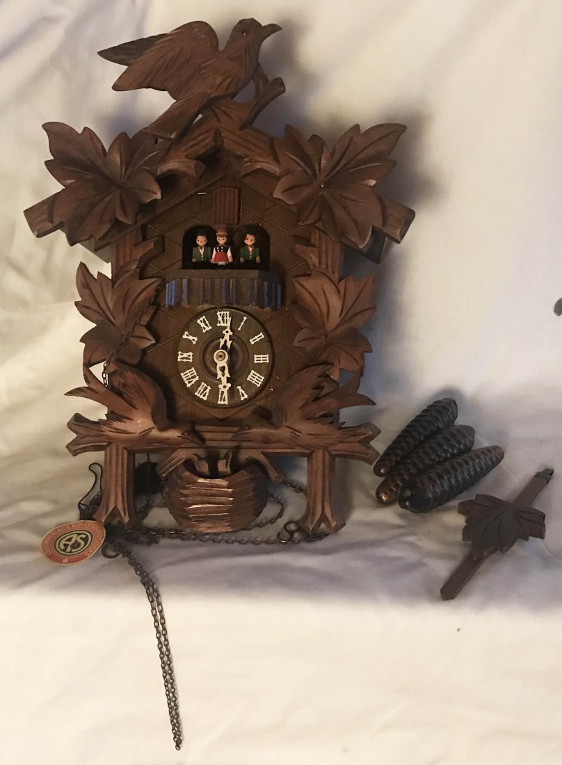 CUCKOO CLOCK: Cuckoo clock w/3 carved birds, leaf design, 2 birds feeding young birds in nest, 4 people rotating, paper/string tag "Original Black Forest Cuckoo Clock", pendulum and acorn shaped weights clock-14 1/