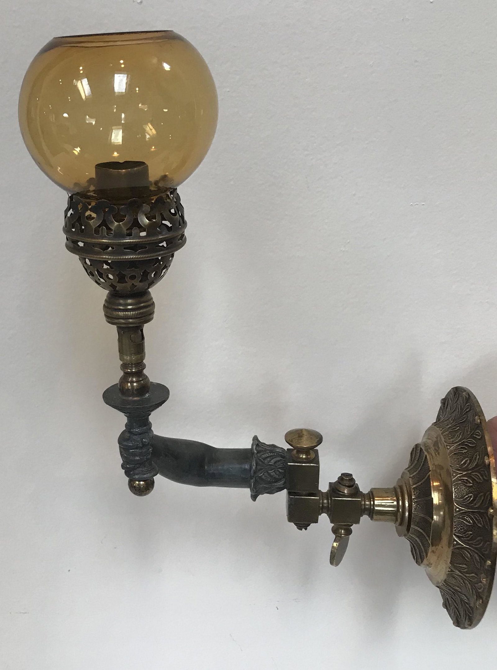 Vintage Cigar Lighter: Vintage gas wall mounted cigar lighter w/brass plate, thumb control handle, 1 hinged bracket, human arm and hand holder w/small amber glass shade; arm/hand in lead/cast metal; glass shade has slight r