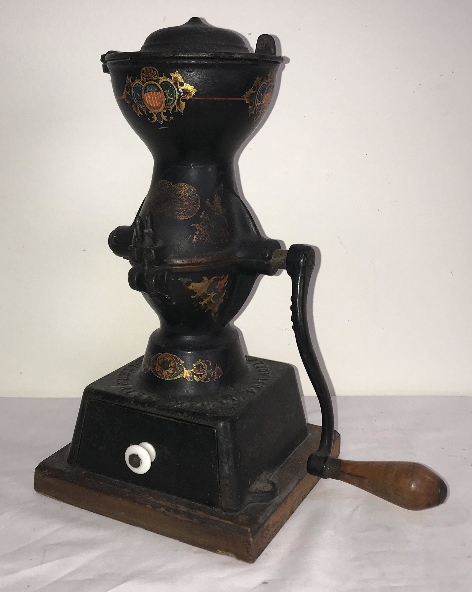 Vintage Cast Iron Coffee Grinder: Vintage cast iron coffee grinder marked Enterprise Mfg. Co., Philadelphia, USA w/crank, round swivel lid at top, base drawer w/white porcelain knob pull, mounted on a wooden base, red, gold and blue A