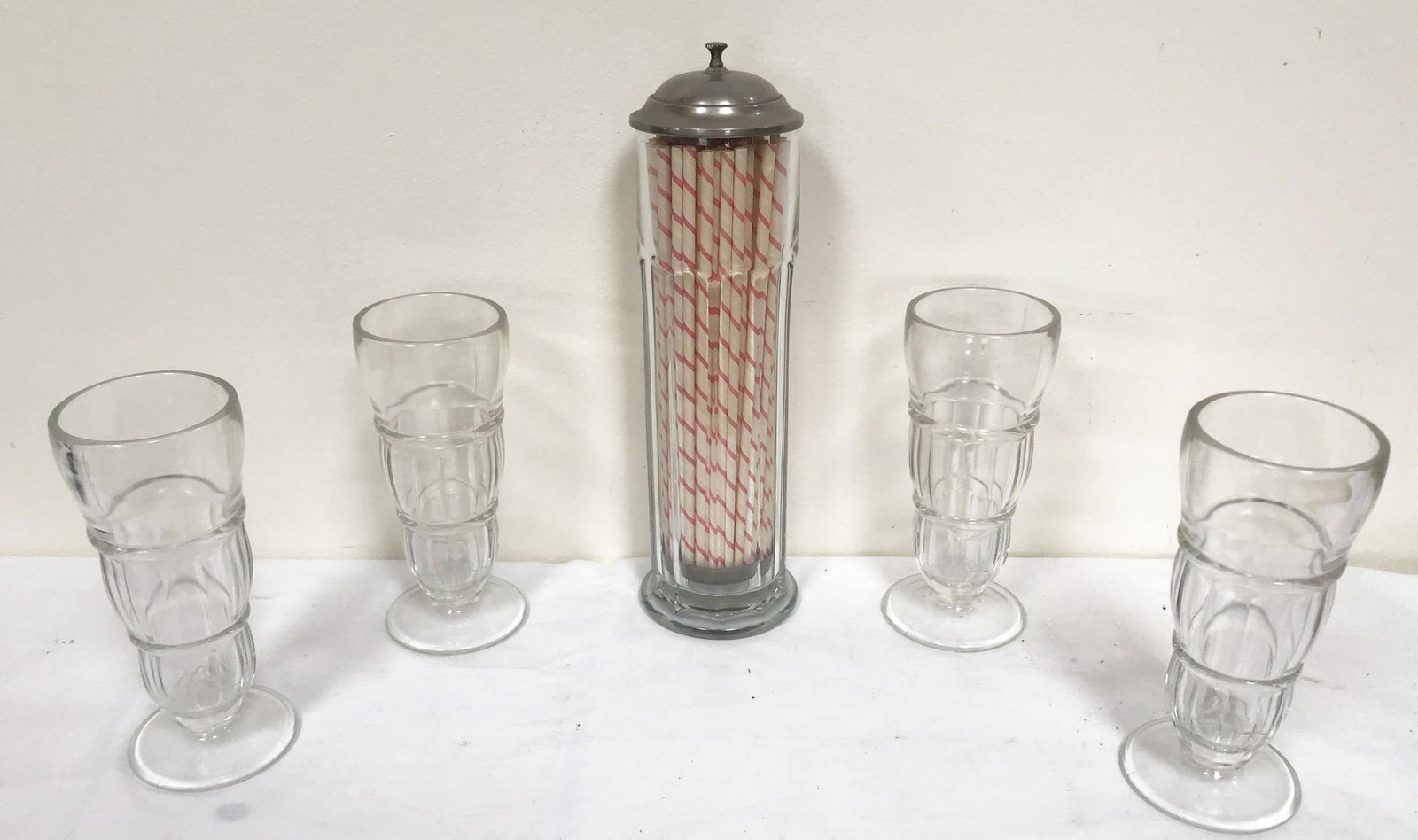 Vintage Soda Fountain Straw Dispenser and Soda Glasses: Vintage clear glass soda fountain straw dispenser, nickel plated lid, rod and base w/white/red stripe paper straws, panel design, 13 1/2" T x 4" base diameter AND (4) clear ice cream soda glasses, eac