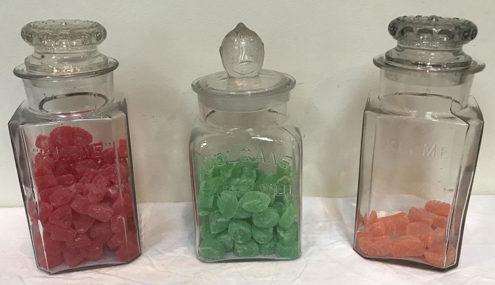 3 Vintage Candy Store Jars: Grouping of 3 vintage clear glass candy store jars: (2) octagonal marked Kis-Me Gum, Louisville, KY w/lids, 11 1/4" T x 4 7/8" square and 11" T x 4 7/8" square; (1) marked Colgans Taffy-Tolu", lid w/c