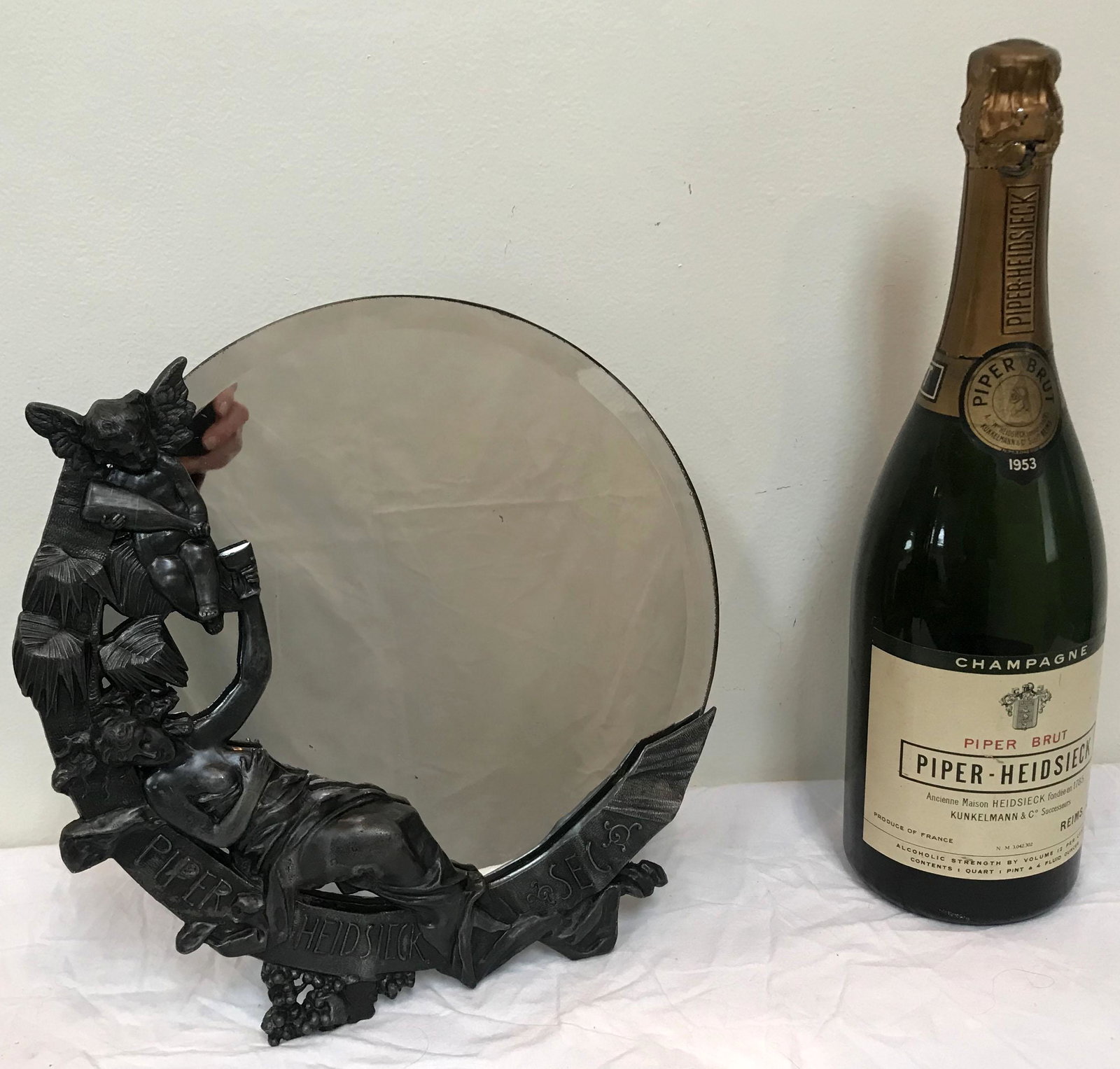 Vintage Advertising Lot: Vintage advertising lot: Art Nouveau style standing mirror w/die cast/white metal holder, figure of a reclining partially nude lady holding a wine cup w/winged cherub pouring from a bottle into a glas