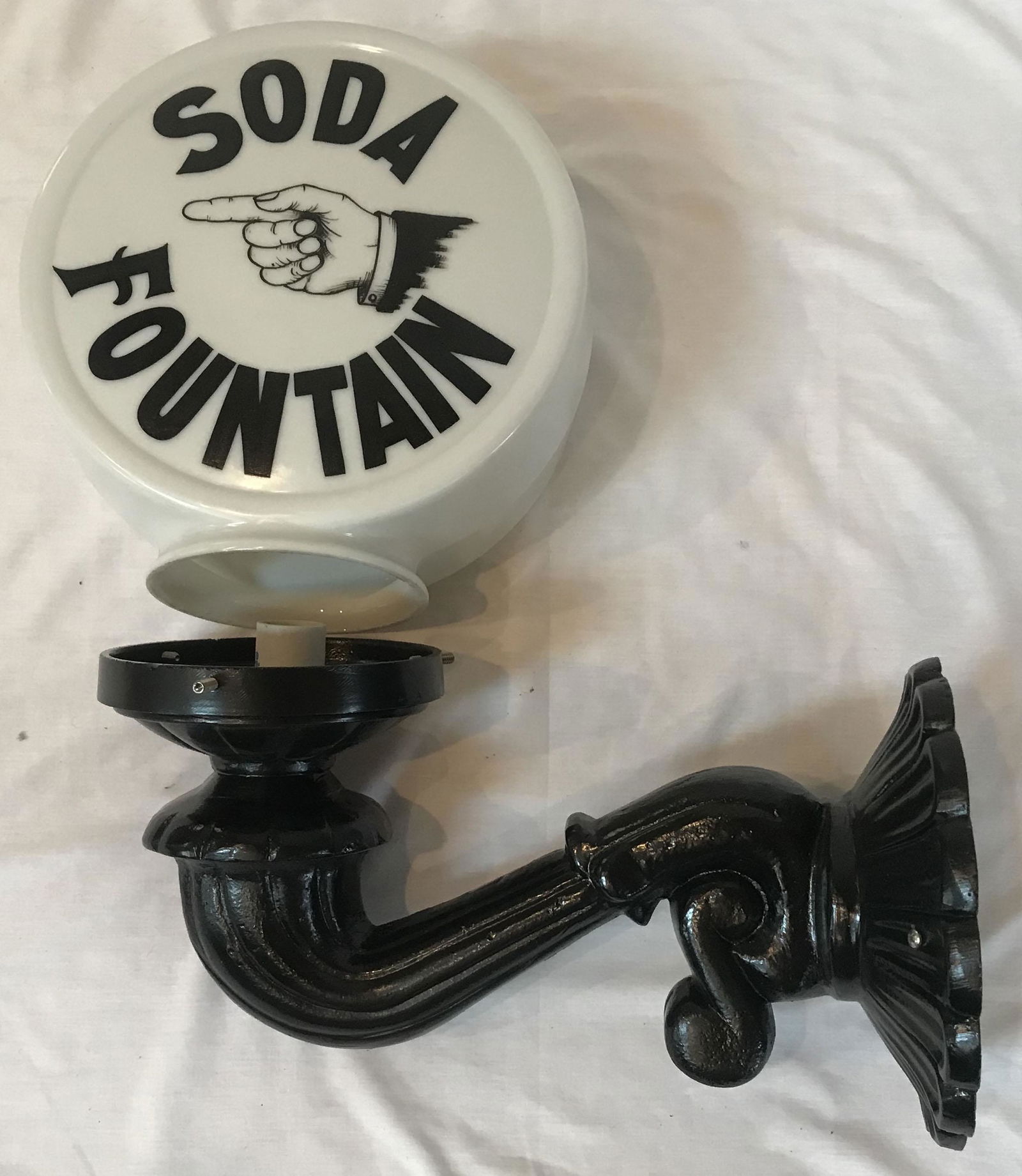 Vintage Soda Fountain Advertising Lamp: Vintage soda fountain advertising wall mounted lamp having a round milkglass shade marked Soda Fountain w/man's hand, index finger pointing left in black paint mounted on a reproduction cast metal bra